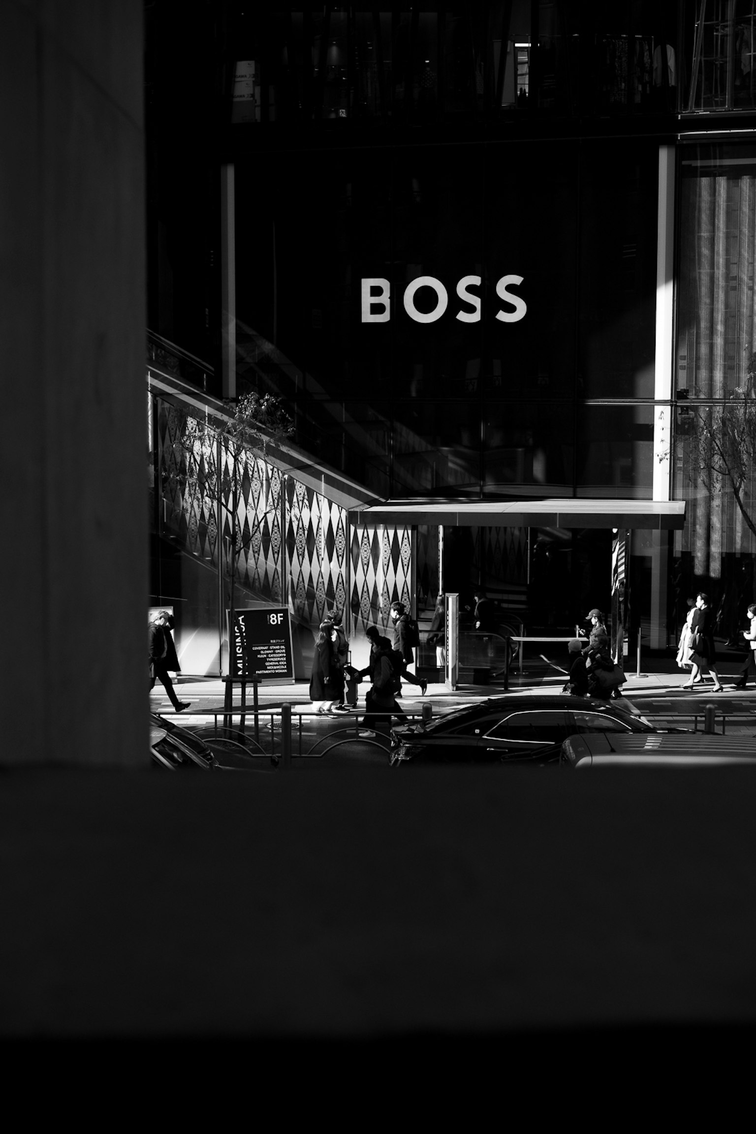 黒と白の都市風景にあるBOSSの看板と通行人