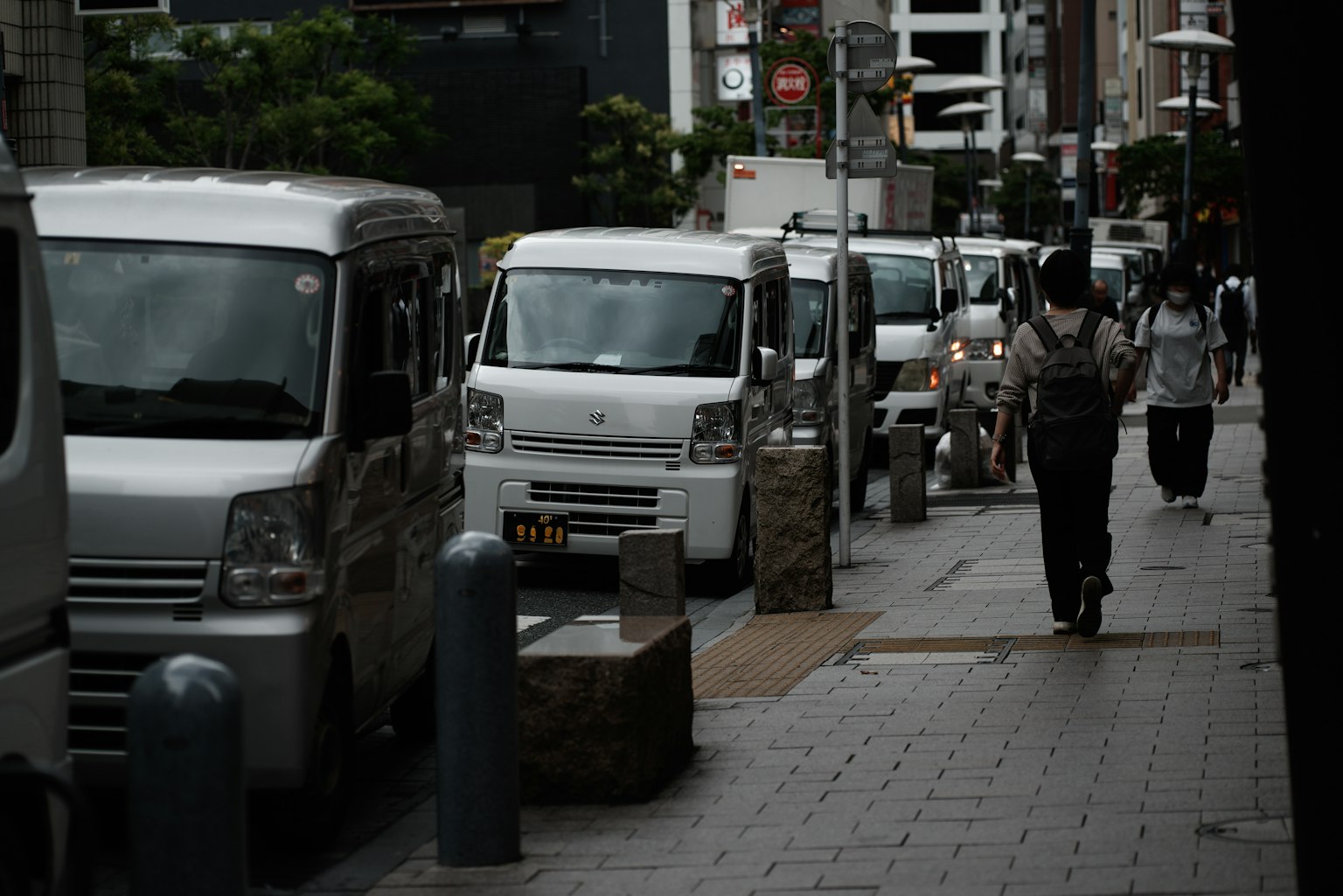 Row of white vans lined up on an urban street with pedestrians
