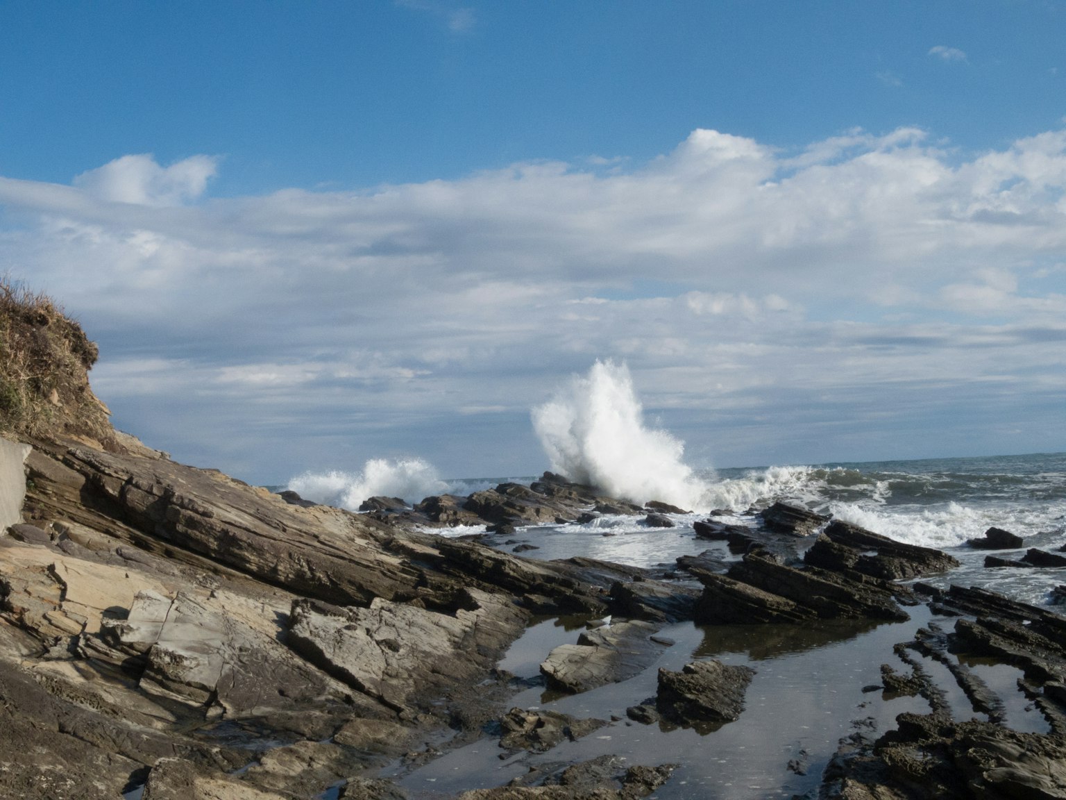 Waves crashing on rocky shore under a blue sky