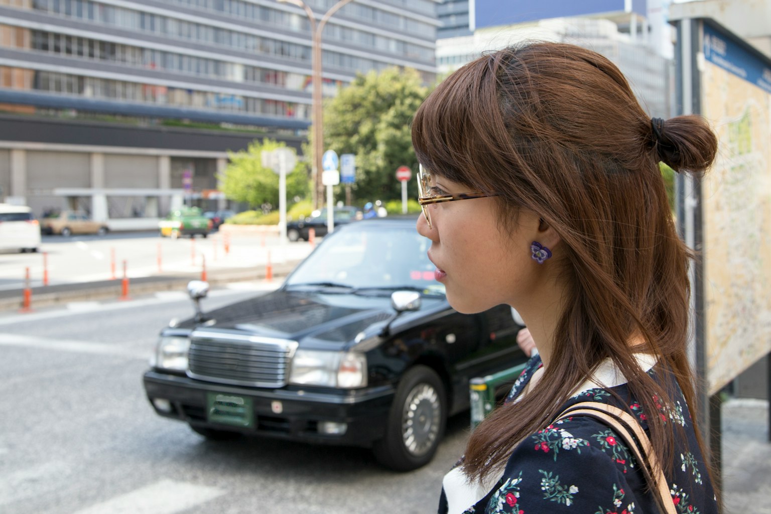 Side profile of a woman in front of a black taxi with cityscape and modern buildings in the background