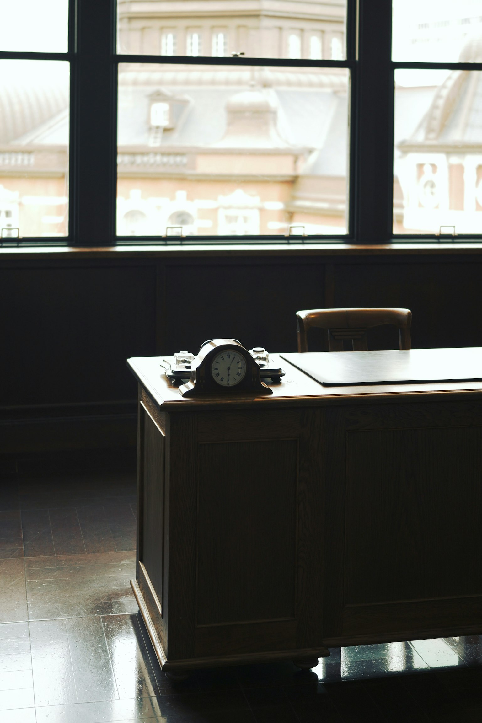 Bureau en bois et chaise dans une pièce faiblement éclairée avec de grandes fenêtres montrant une vue extérieure