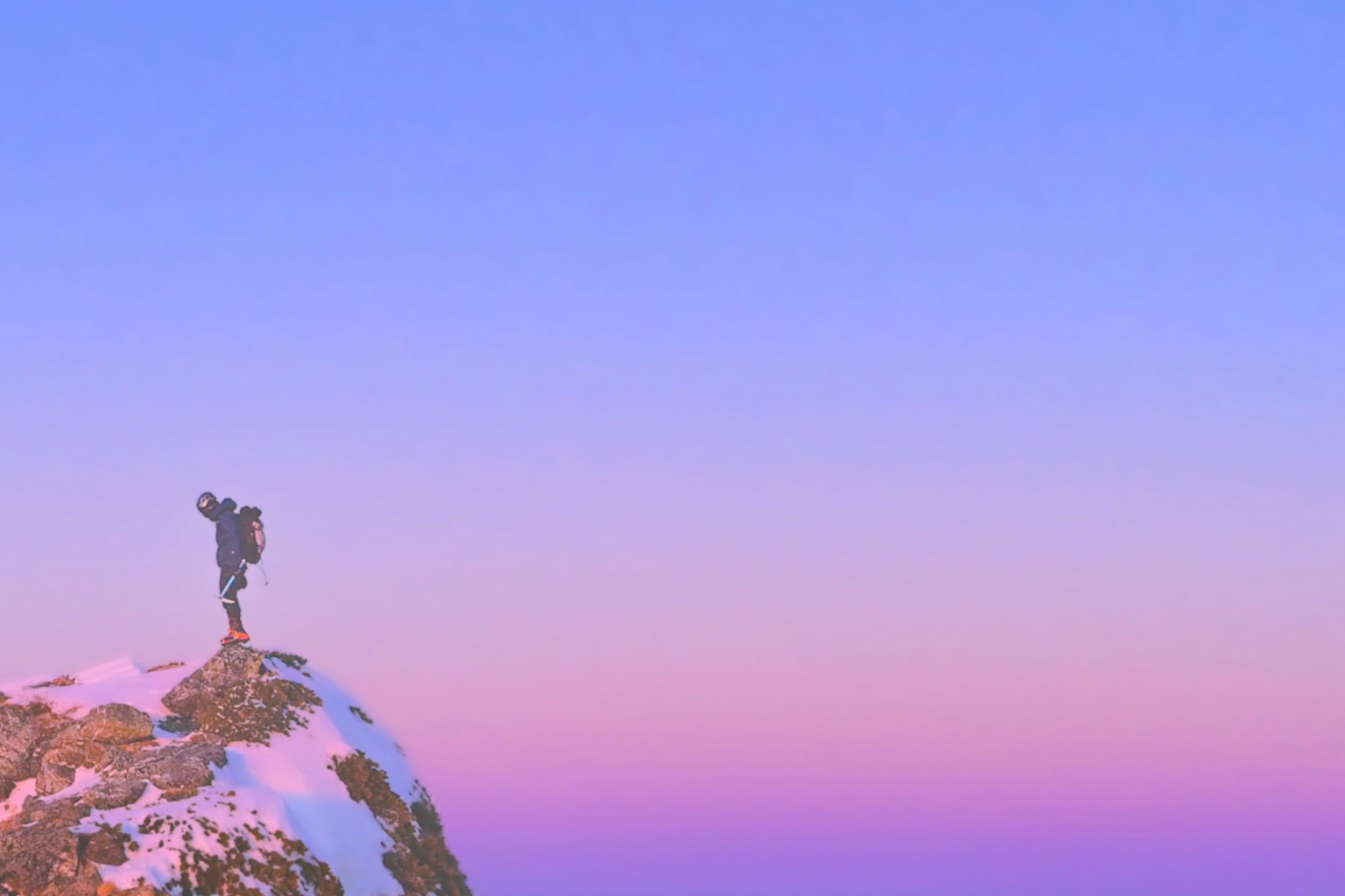 Siluet seseorang berdiri di puncak gunung bersalju dengan langit biru-pink lembut