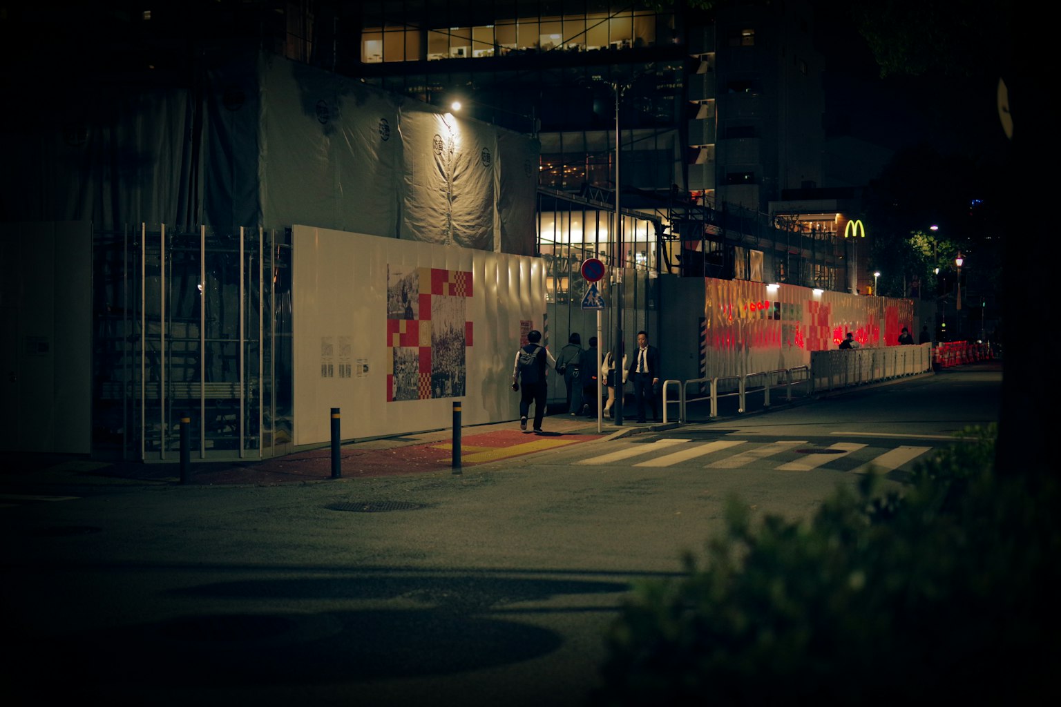 夜晚街景，人们走过一面有红色装饰的墙