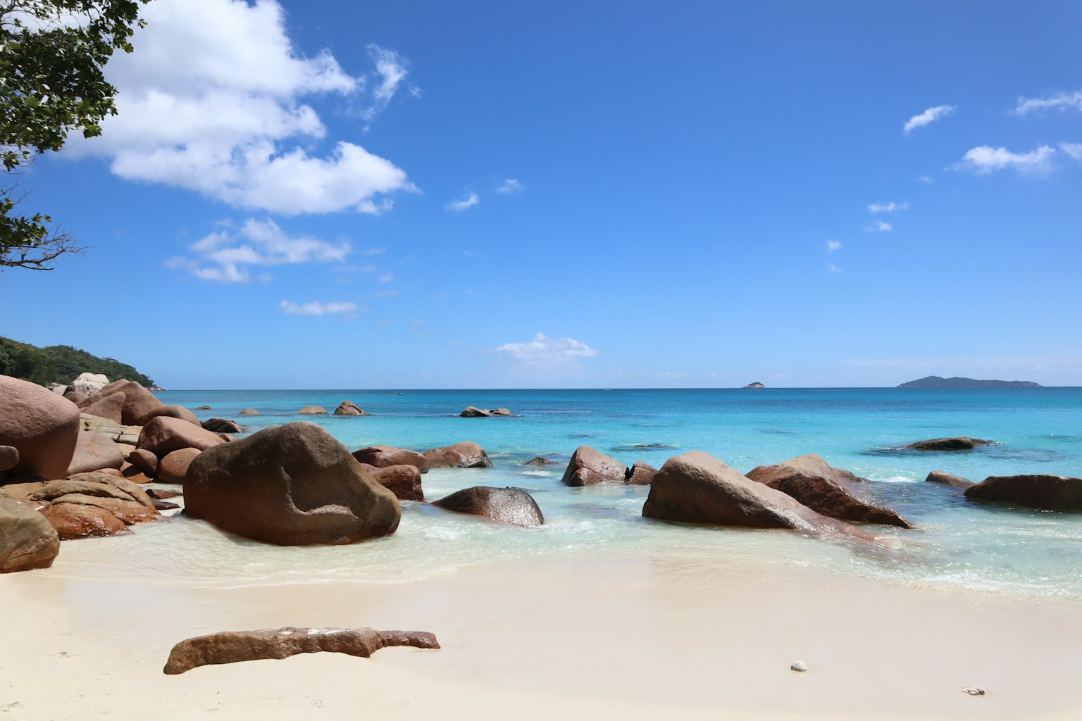 Scenic beach view with calm sea and blue sky featuring large rocks and white sandy shore