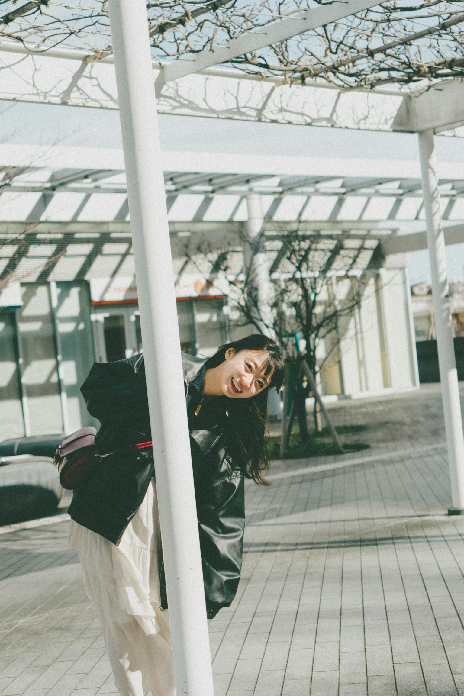 A woman peeking from behind a pole smiling in bright sunlight