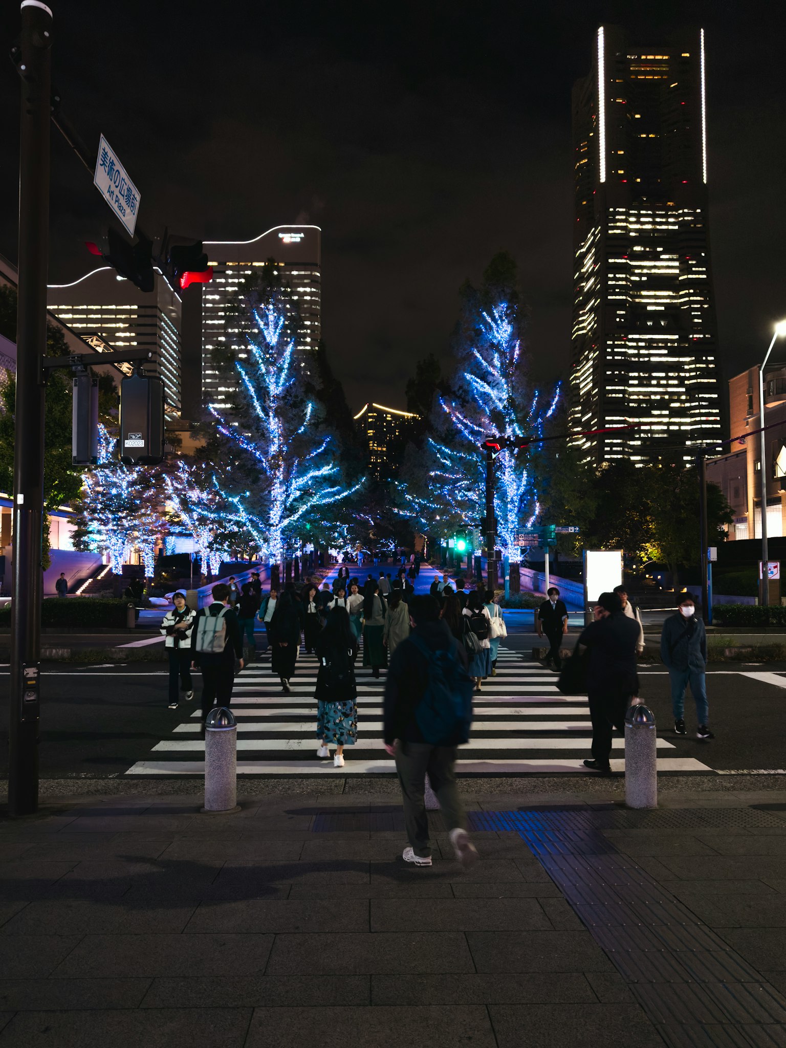 Intersection with people walking under illuminated blue trees at night