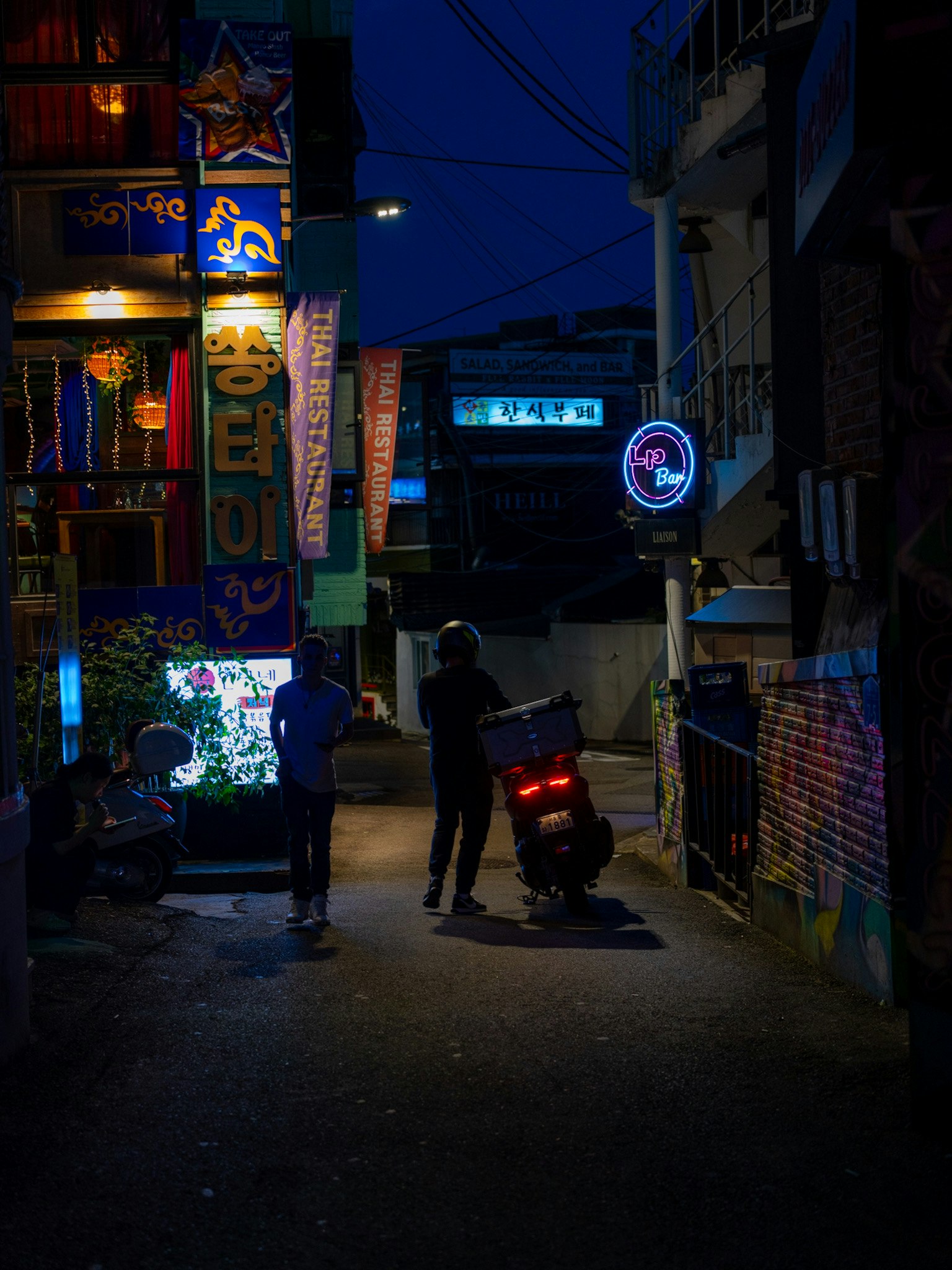 Des personnes et une moto dans une ruelle nocturne aux enseignes néon