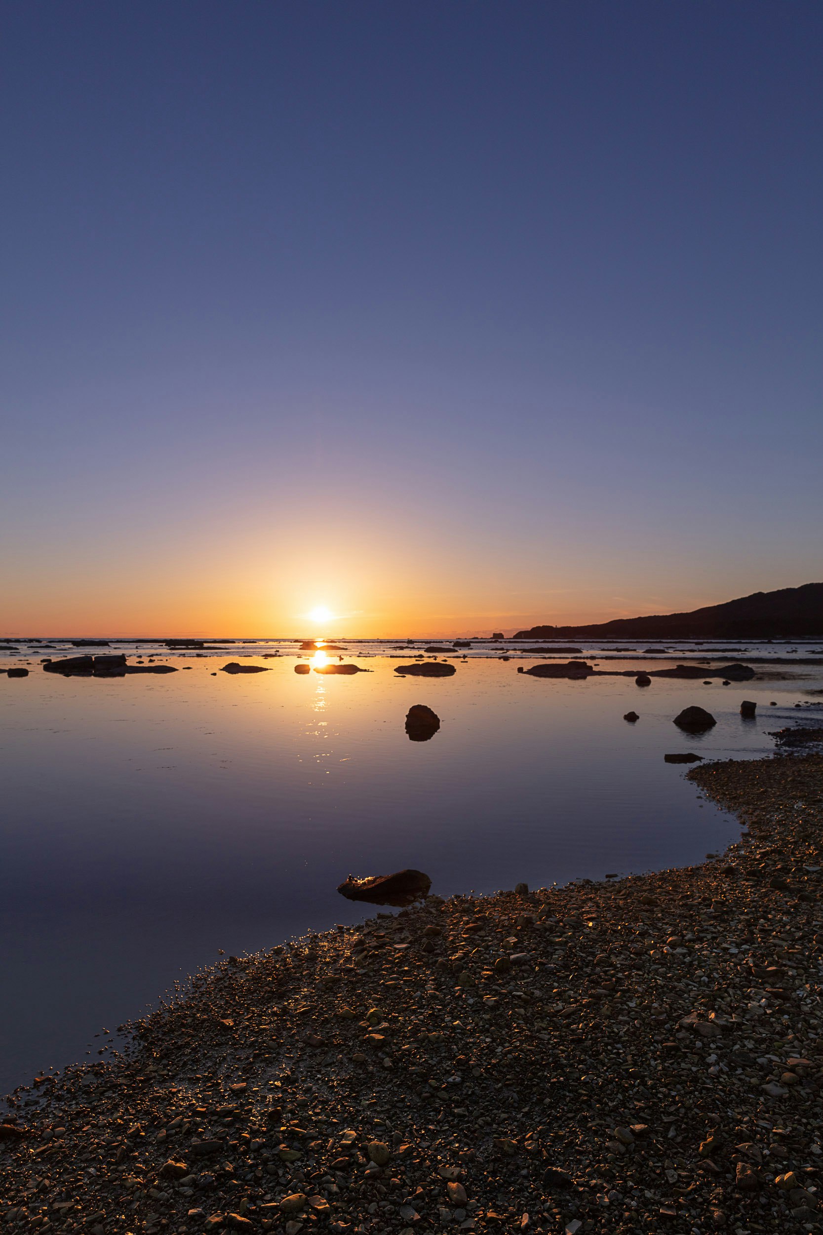 夕暮れの海辺に広がる静かな水面と砂浜の風景