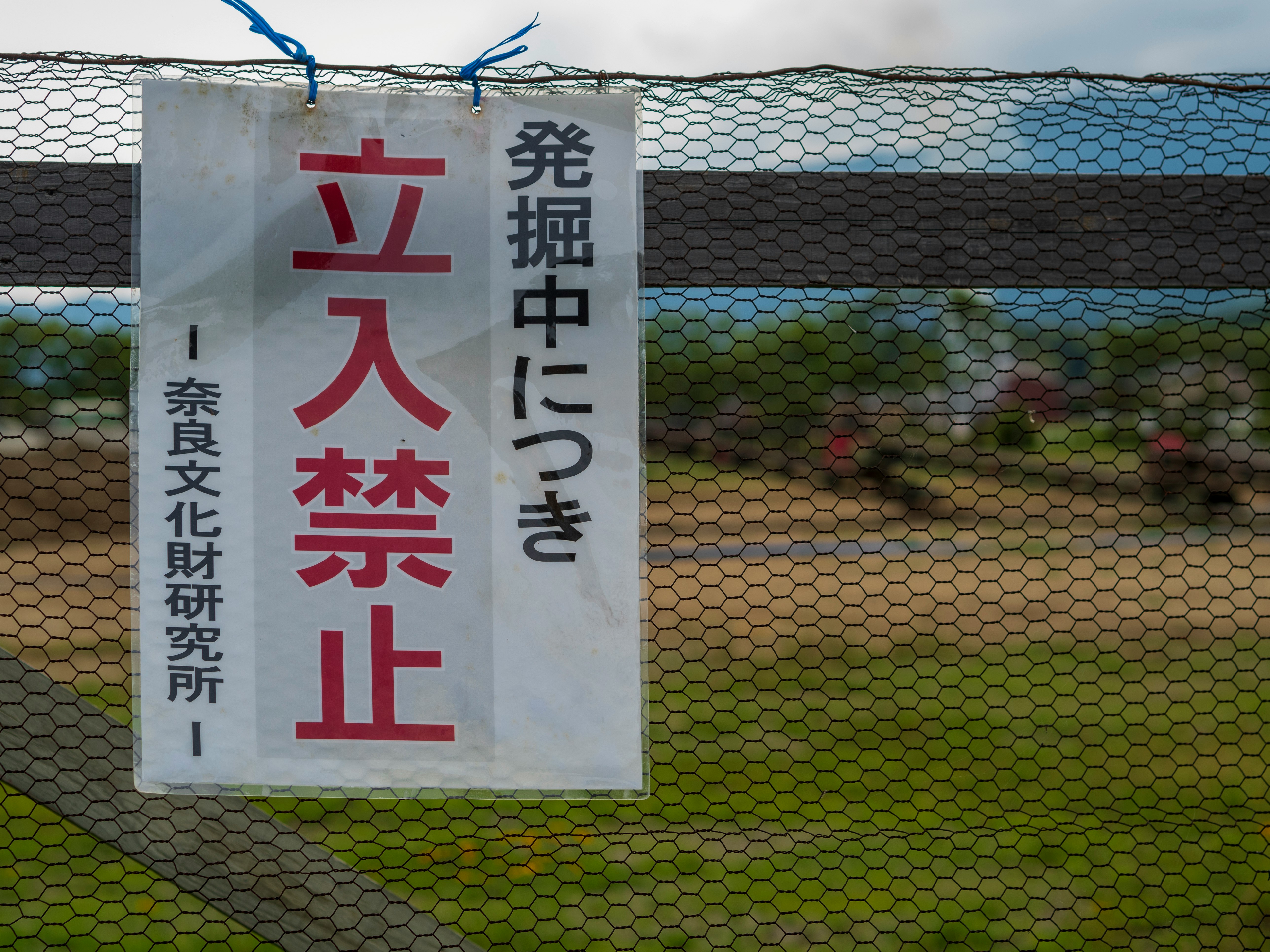 フェンス越しに掲げられた立入禁止の看板と発掘中表示の張り紙