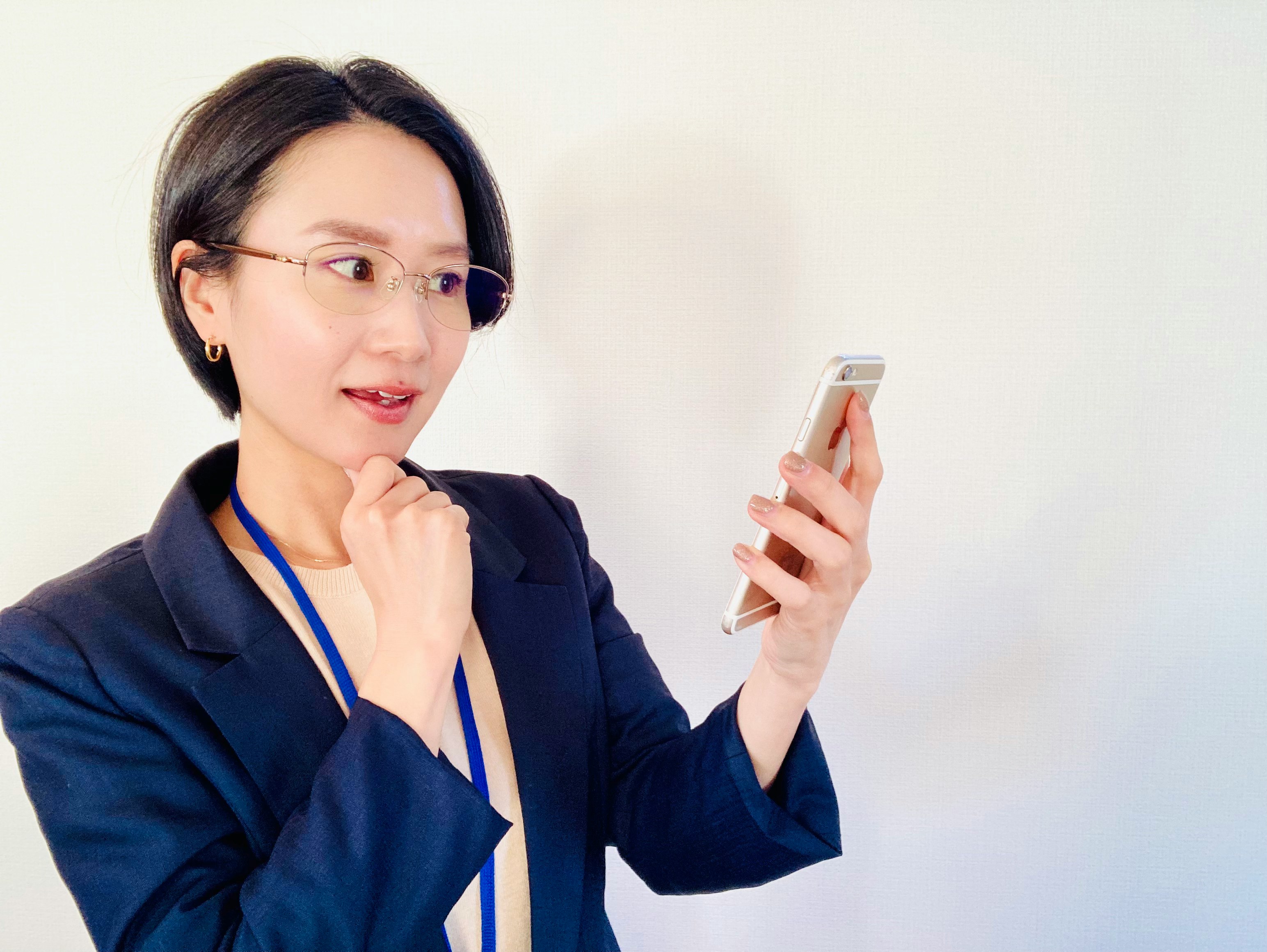 Frau im Business-Anzug, die nachdenklich auf ein Smartphone schaut