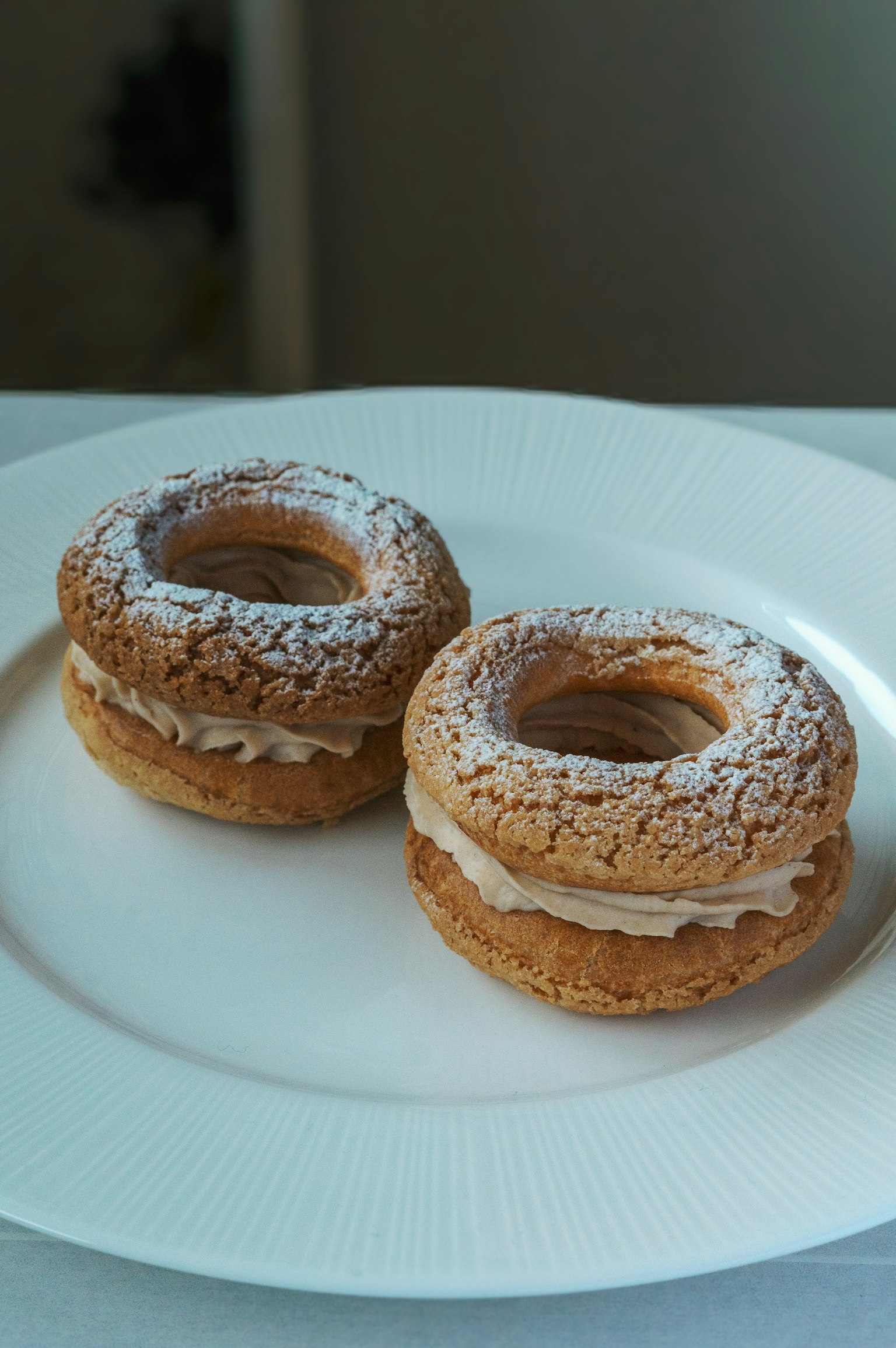 Deux beignets fourrés à la crème saupoudrés de sucre glace sur une assiette blanche