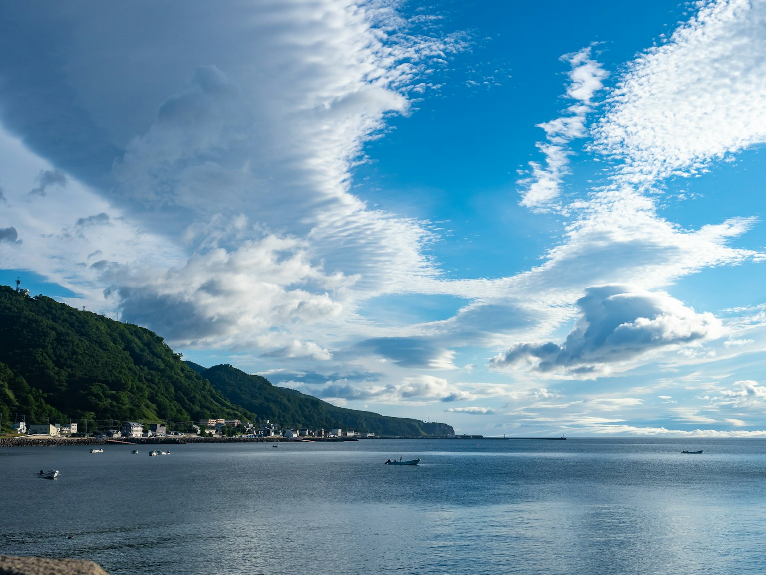 Malerei der See unter einem blauen Himmel mit Wolken, einschließlich Hügel und einem kleinen Dorf