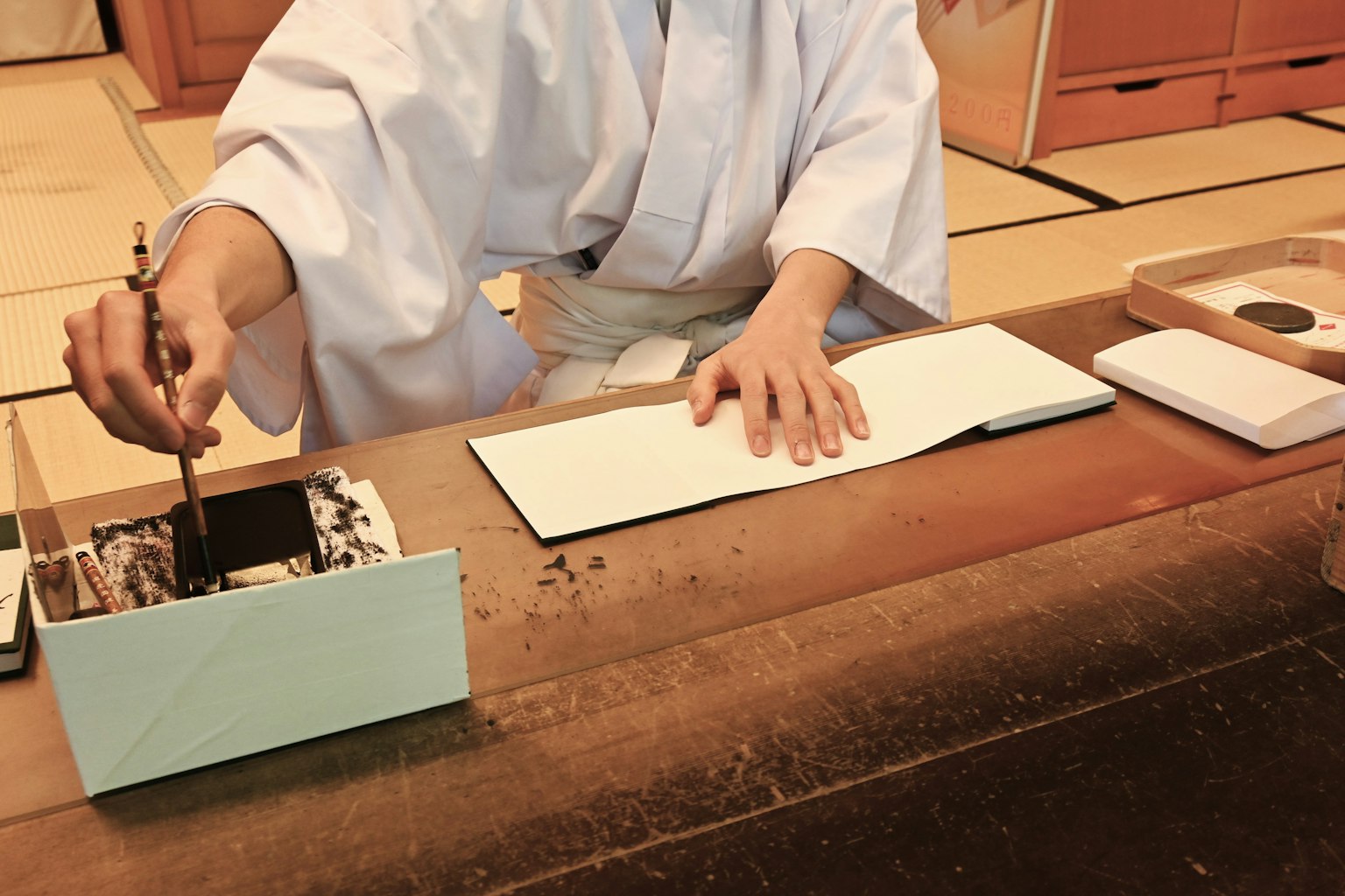 A person in traditional Japanese attire using a brush at a wooden table