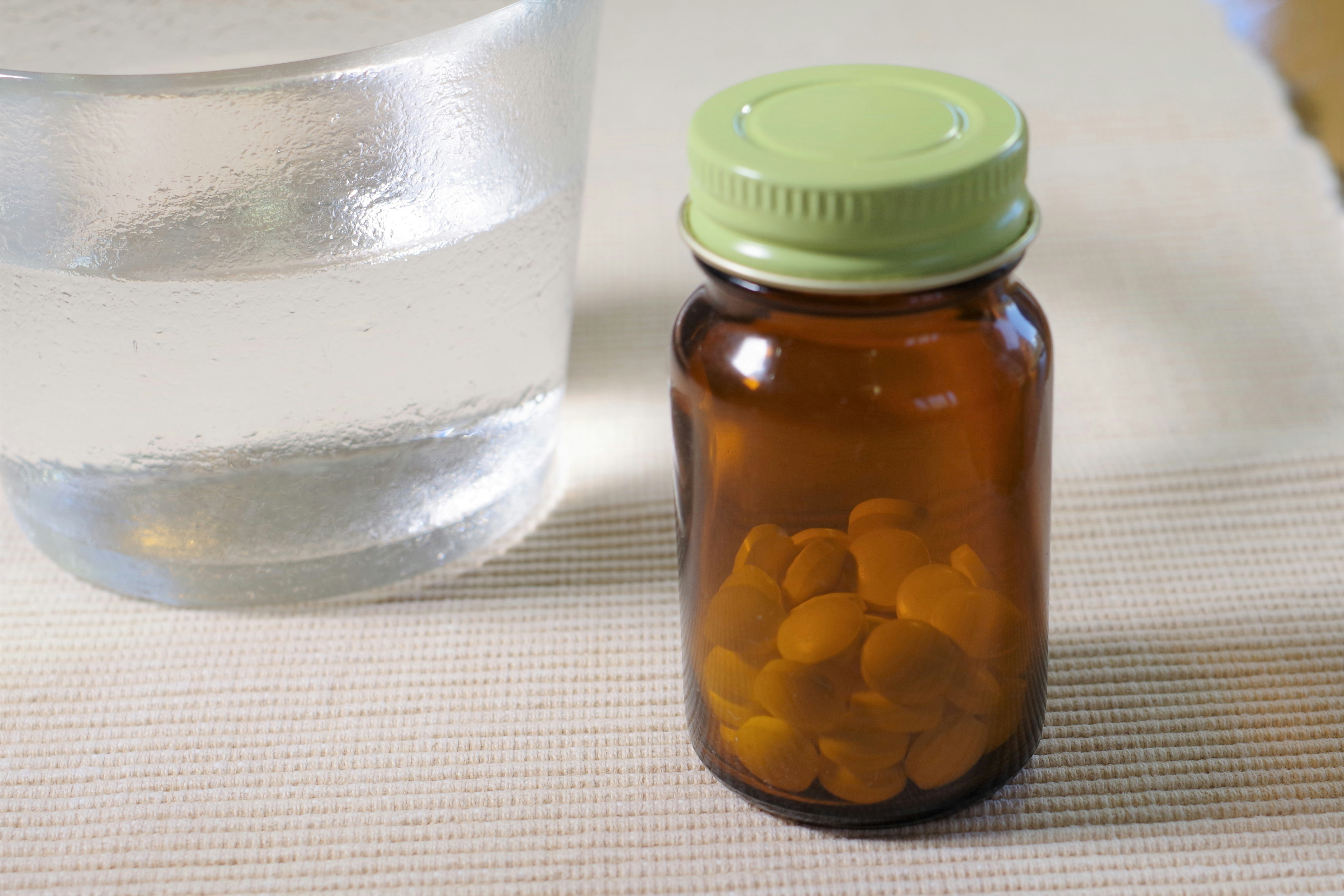vaso de agua junto a un frasco de suplementos