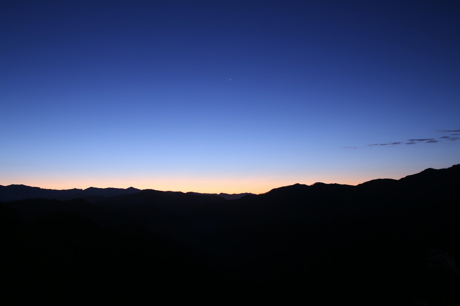 Silhouette of mountains at dawn with a gradient blue sky