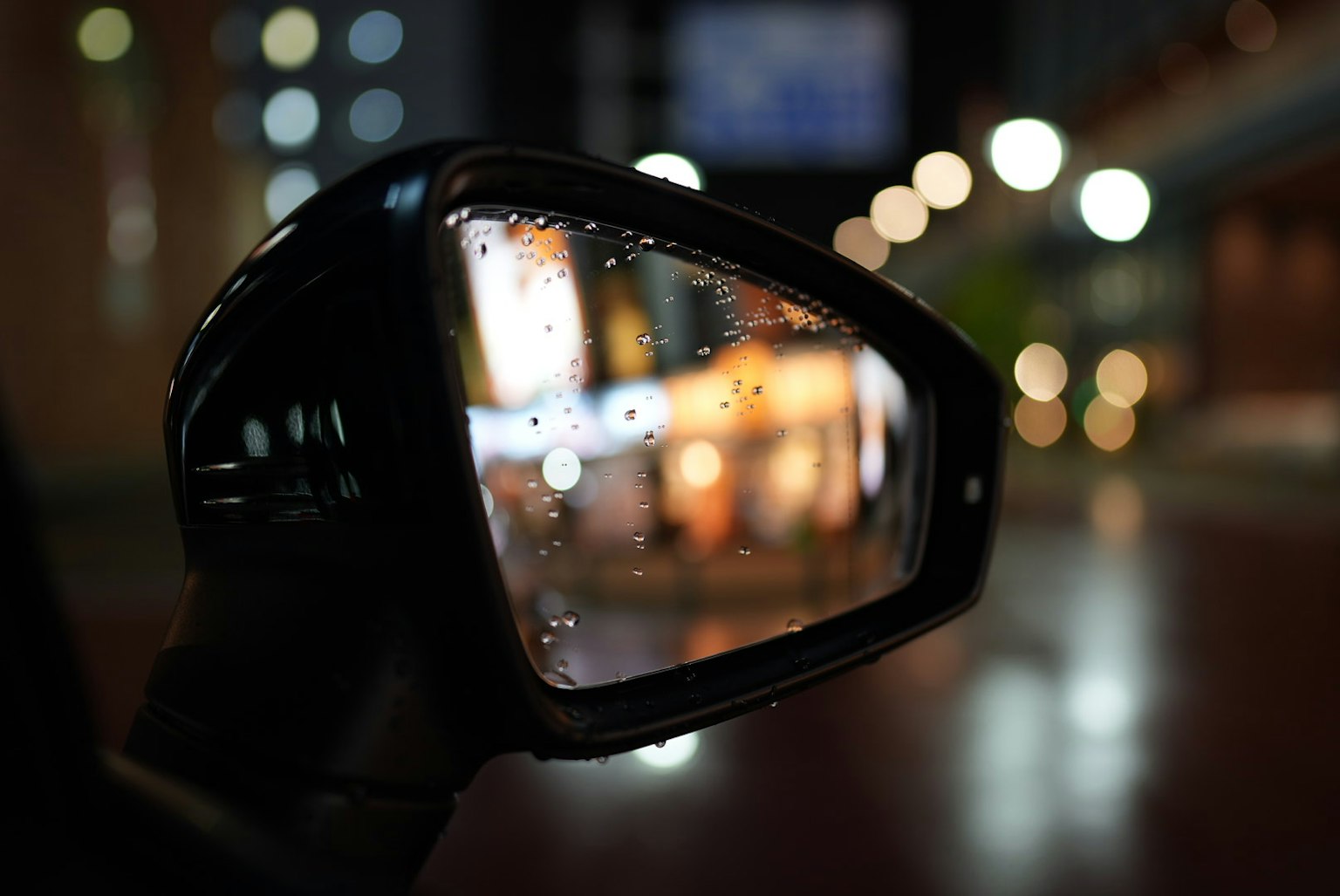 Specchietto retrovisore di auto con gocce di pioggia che riflettono luci cittadine sfocate di notte