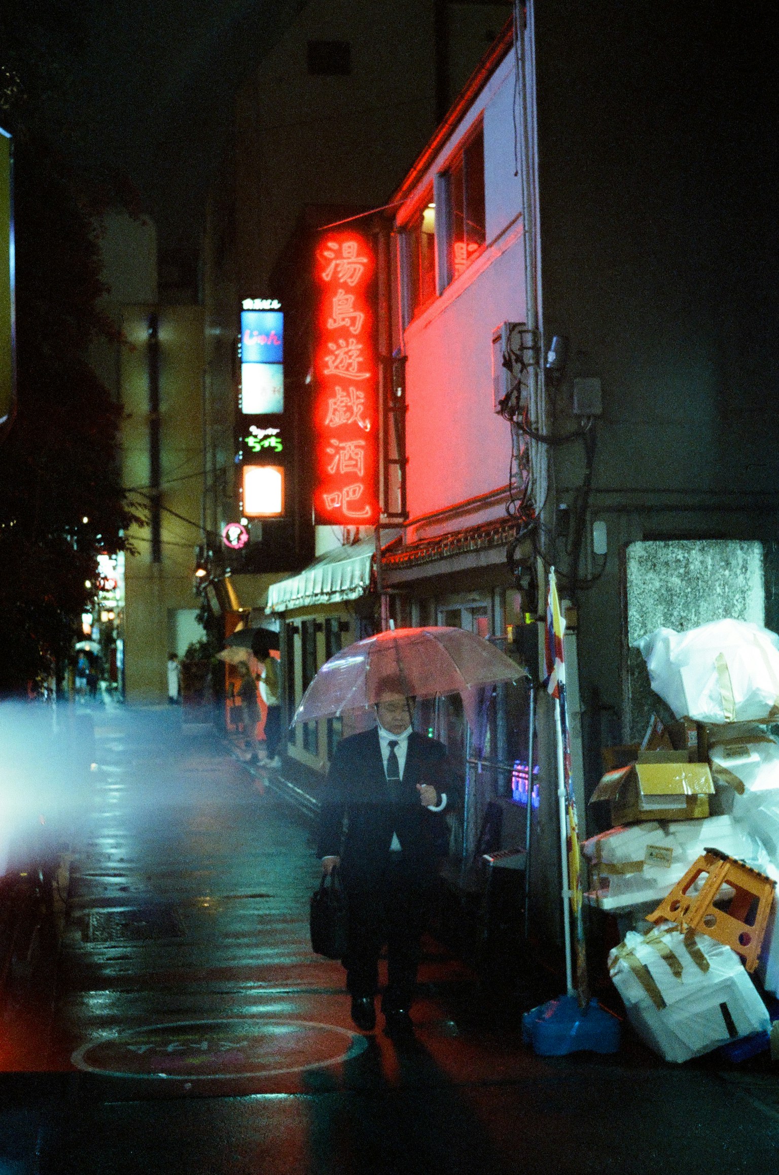 A suited man walking in the rain with neon signs in a nighttime city