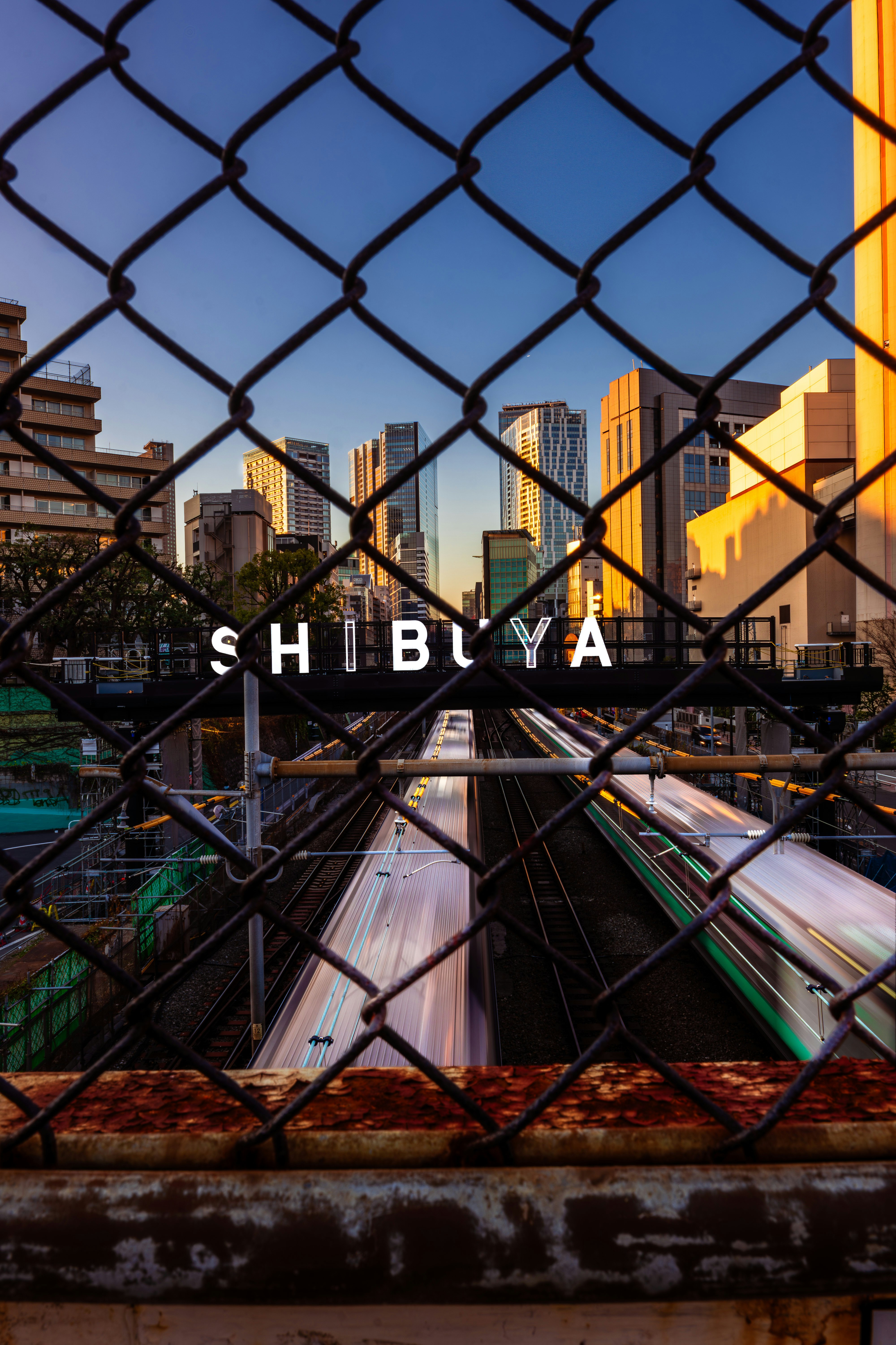 渋谷の都市風景が見える鉄道の写真 フェンス越しに高層ビルと列車が見える