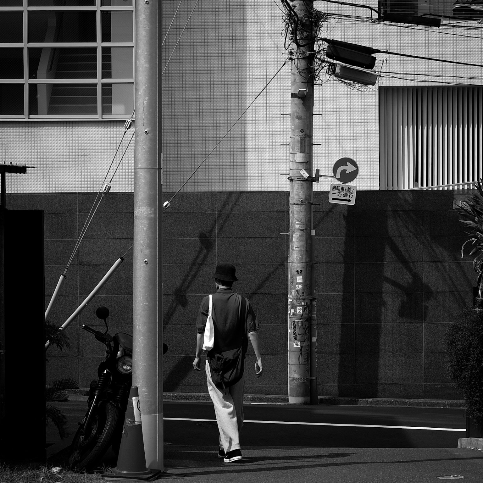 Una persona che cammina in un contesto urbano in bianco e nero con un palo della luce