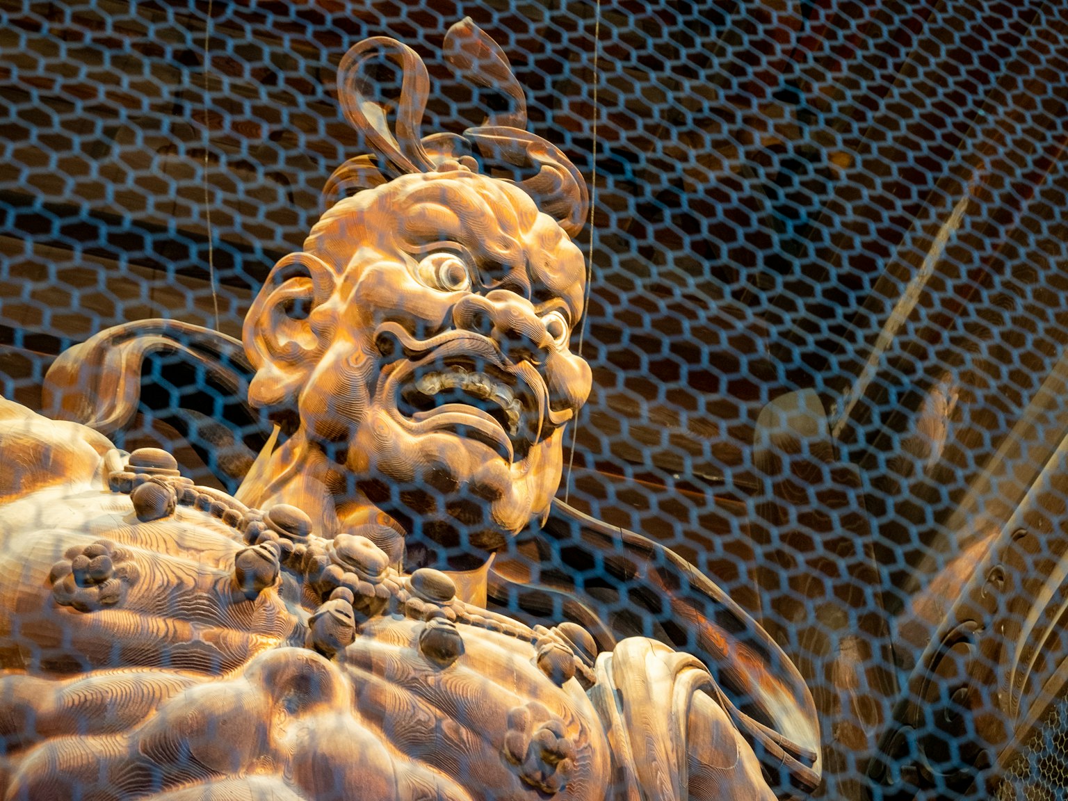 Wooden sculpture of a temple guardian with an angry expression intricate woodwork and a mesh background