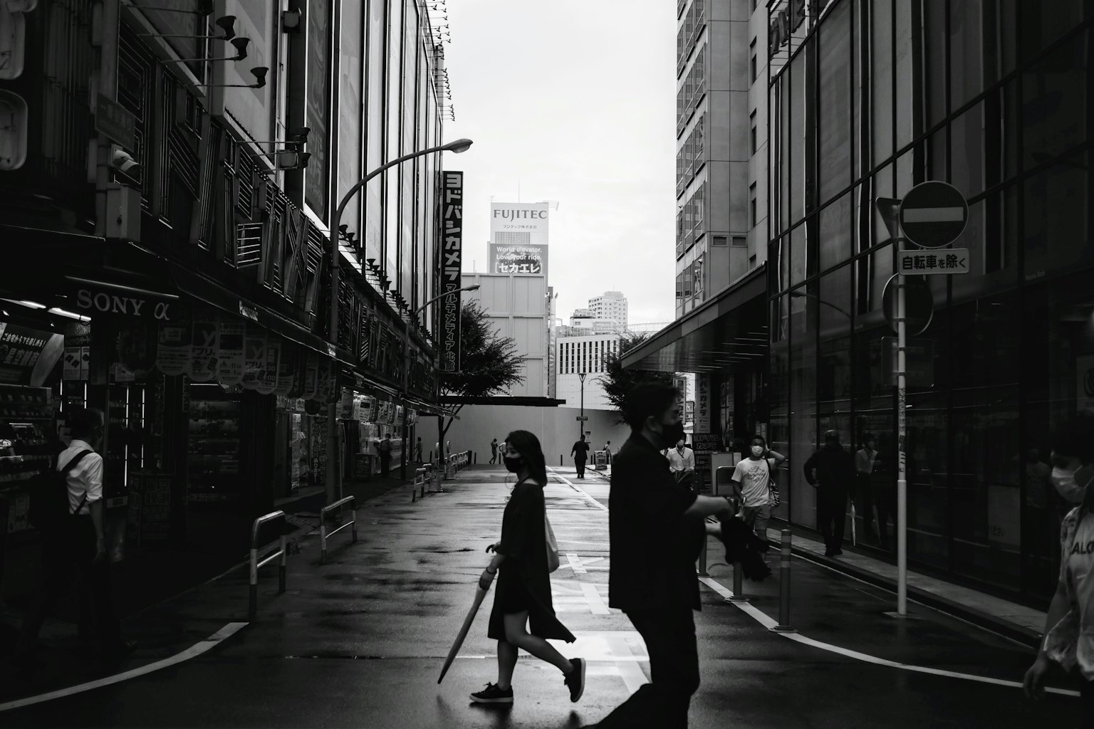 Two figures crossing a rain-soaked street corner with surrounding buildings