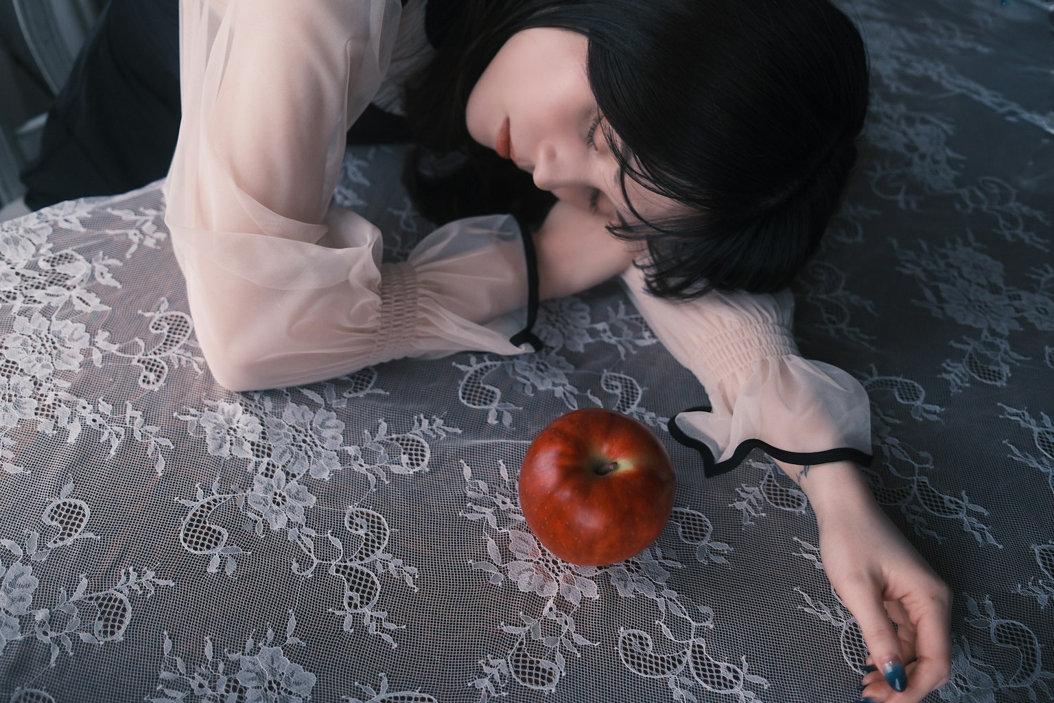女性がテーブルの上で横たわり、赤いリンゴが近くに置かれているシーン
