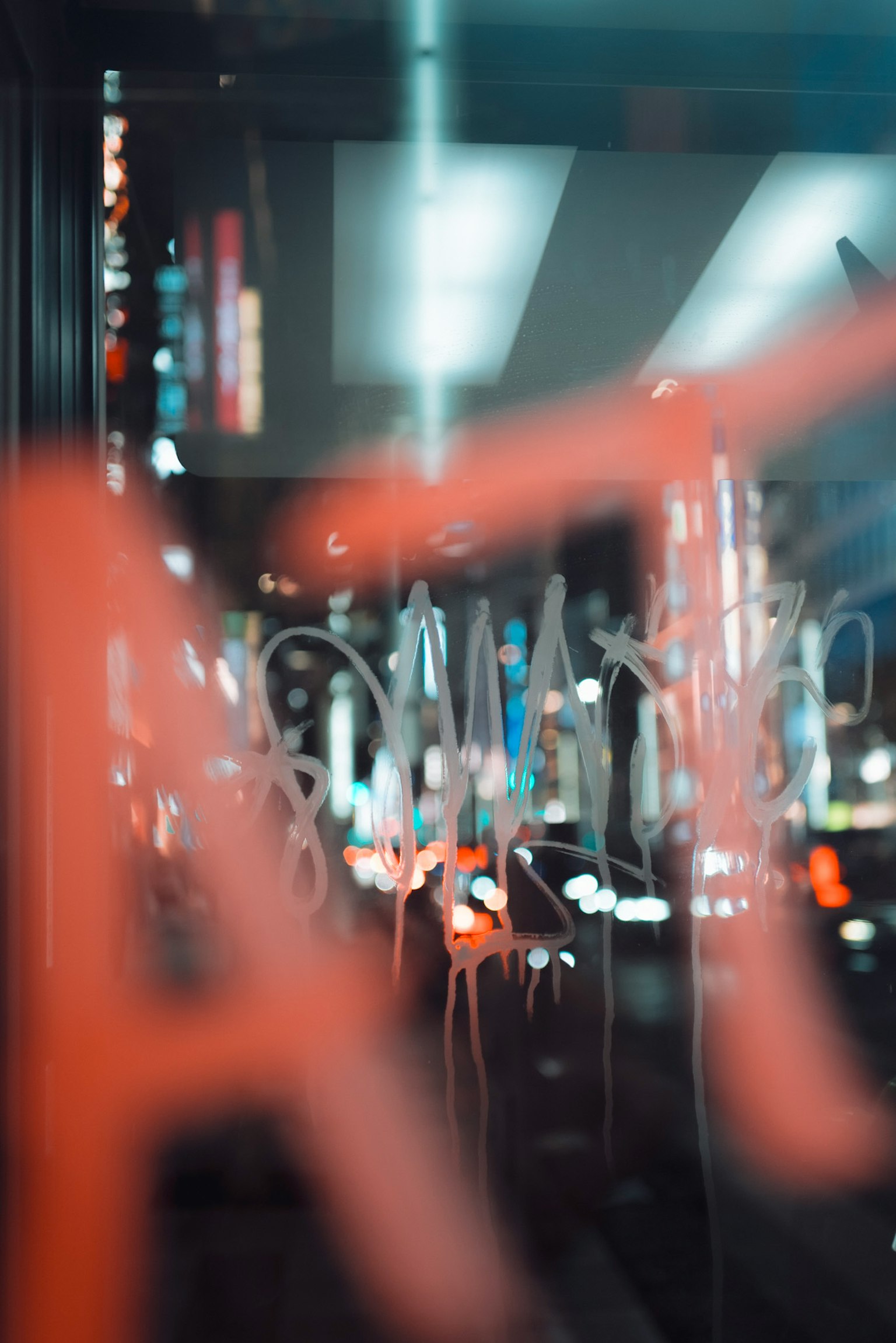 ぼやけたガラスに描かれた文字と夜の都市の明かりが映る