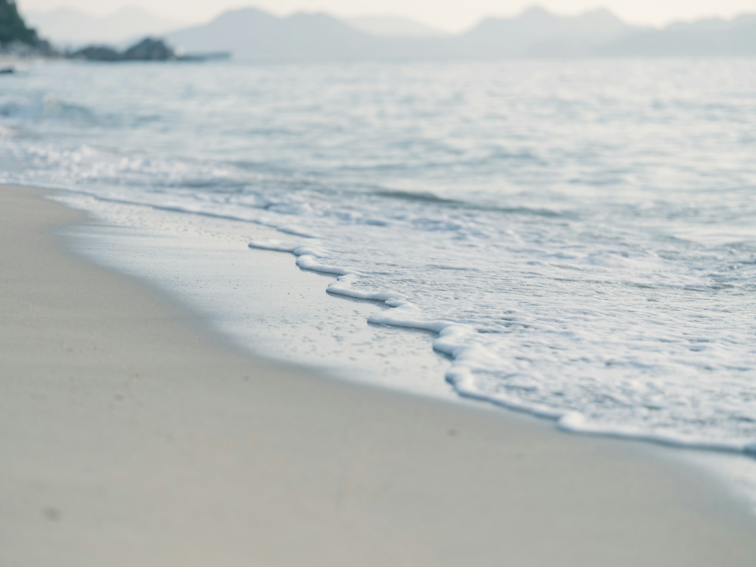 Garis pantai yang tenang dengan ombak lembut menyentuh pasir