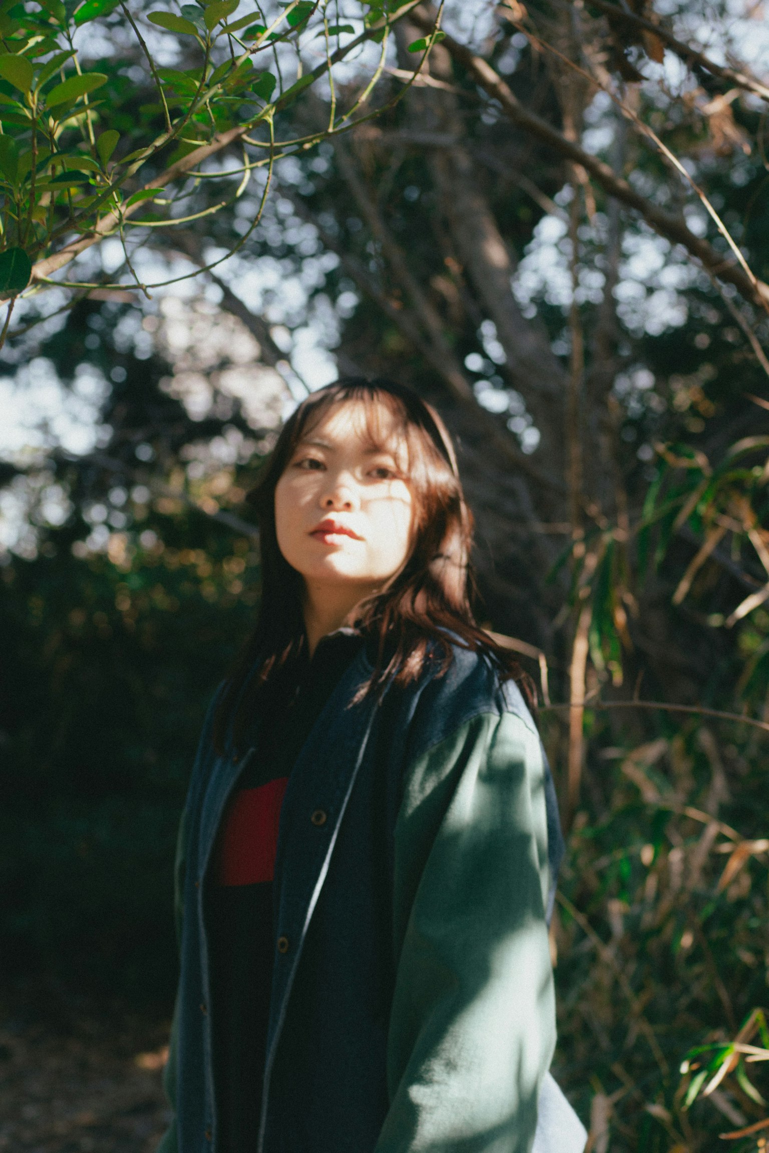 Woman in a green coat standing in sunlight surrounded by greenery