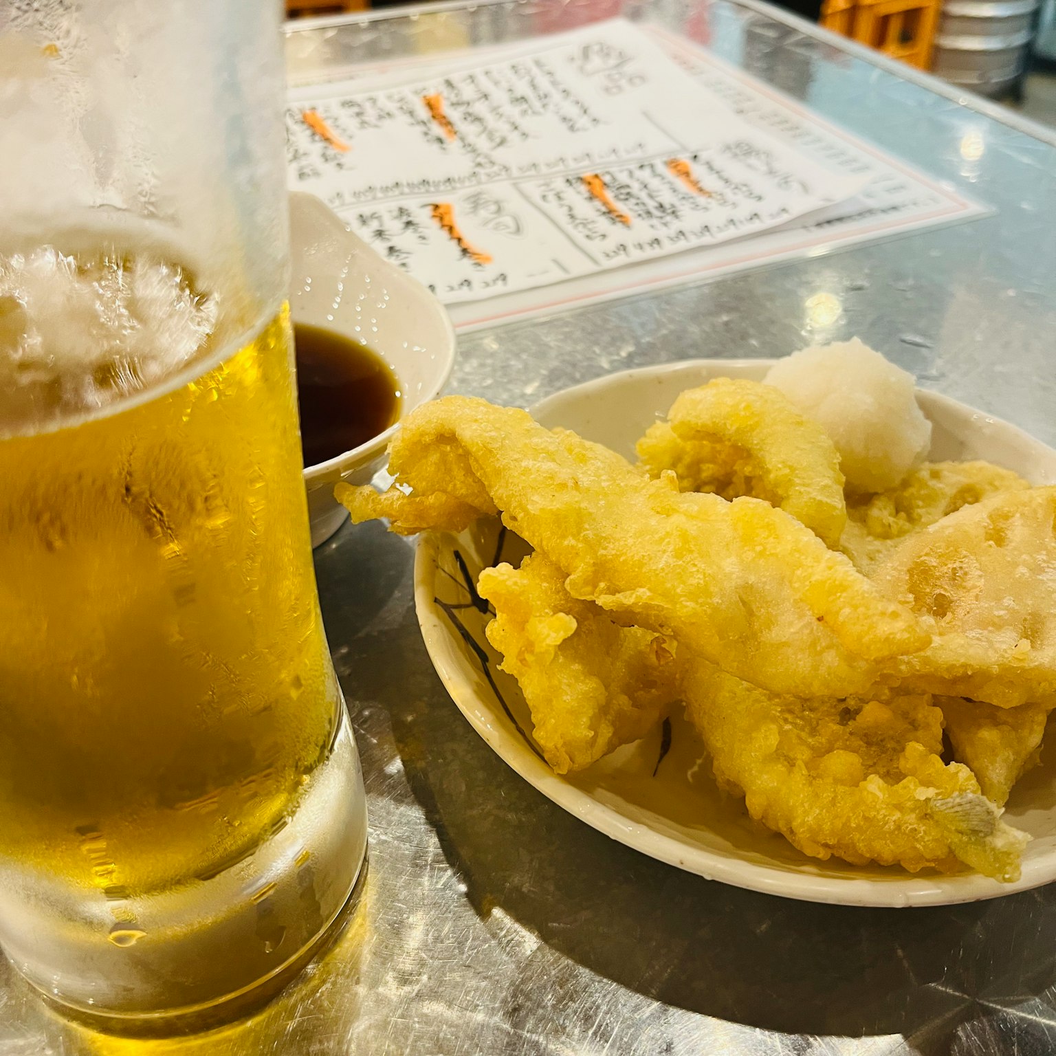 Una escena de comida con un vaso de cerveza y un plato de tempura en una mesa