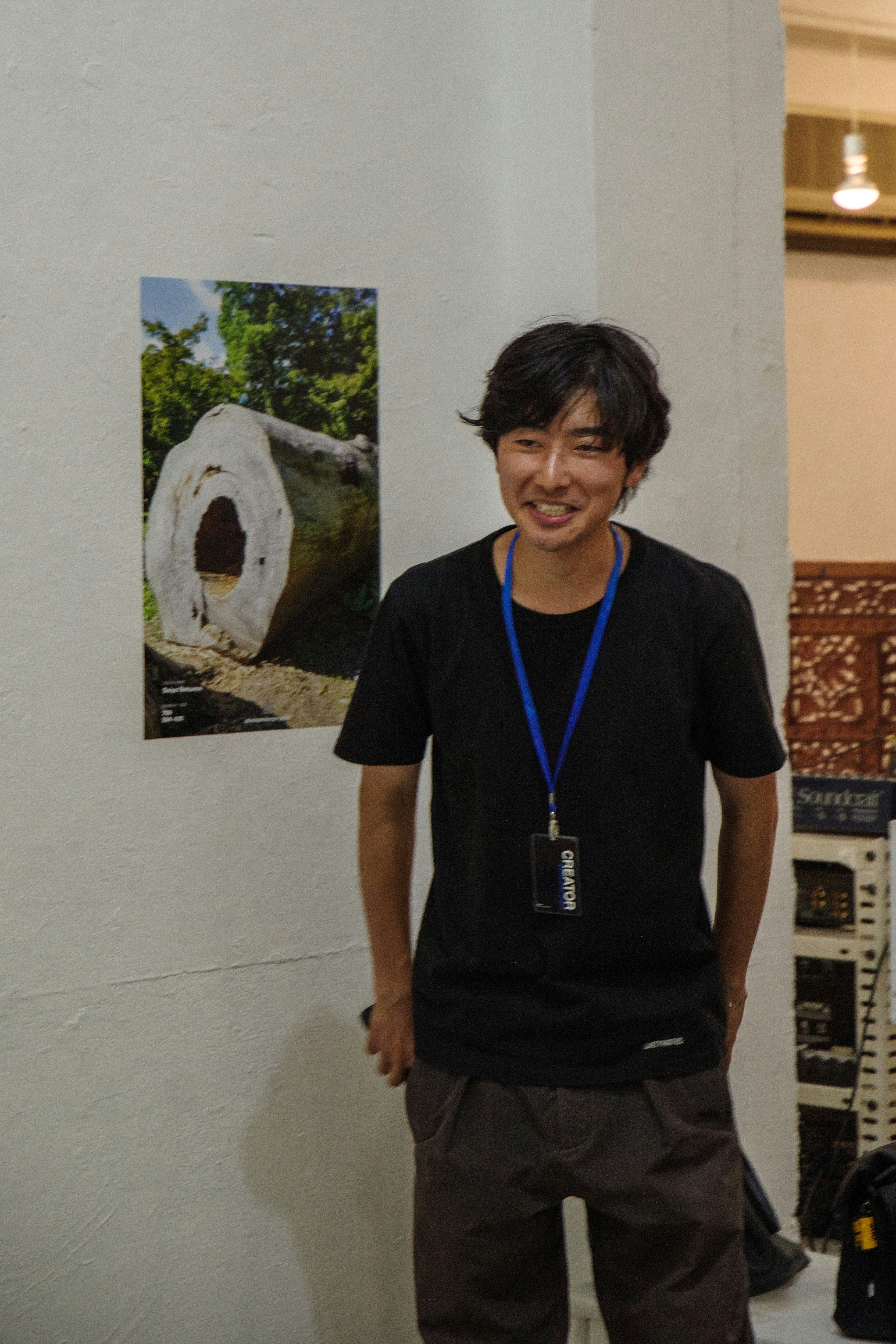 東京のギャラリーで笑顔の男性と展示ポスターのある壁面