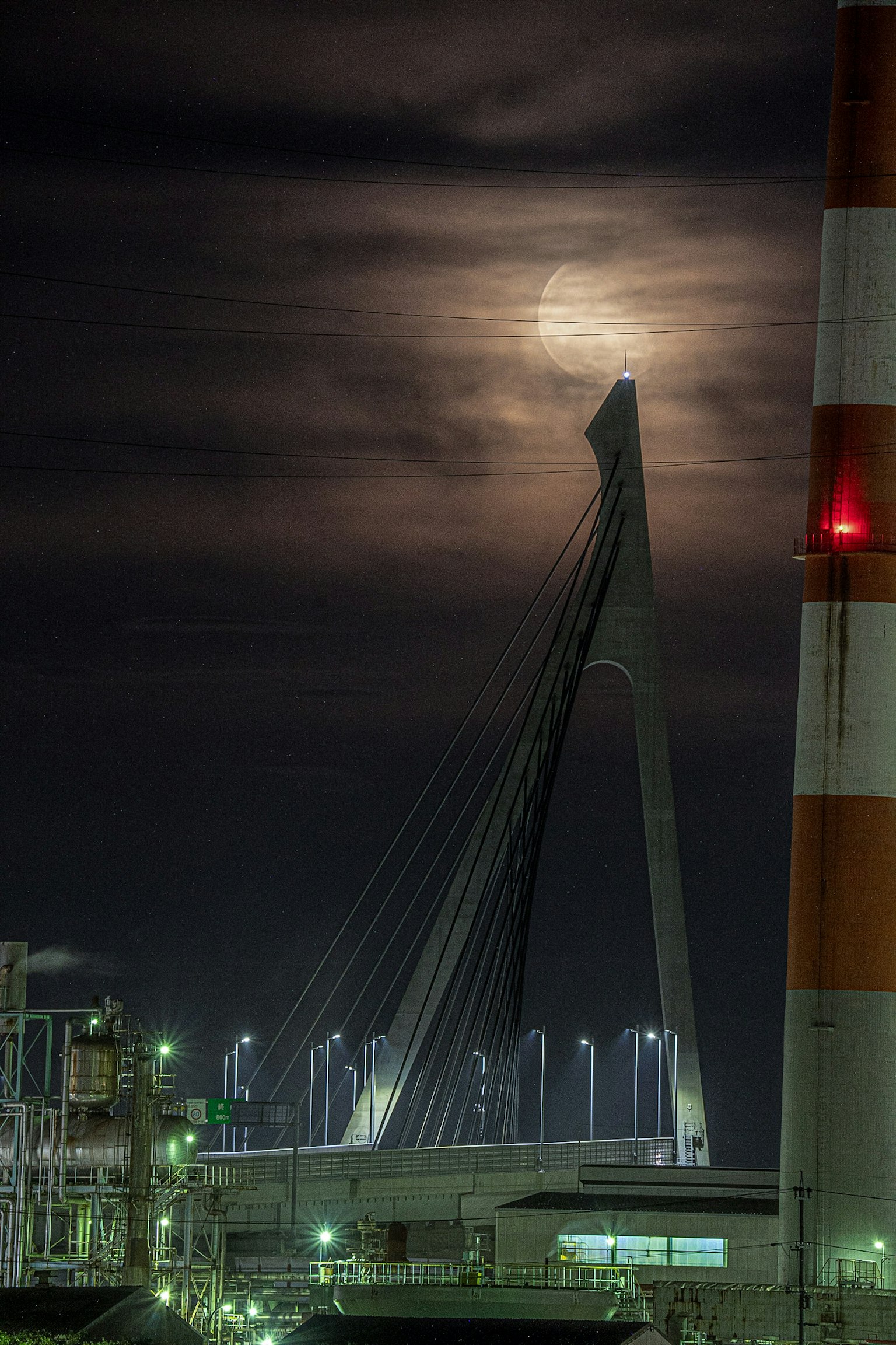 Silhouette d'un pont suspendu contre la lune dans une zone industrielle la nuit