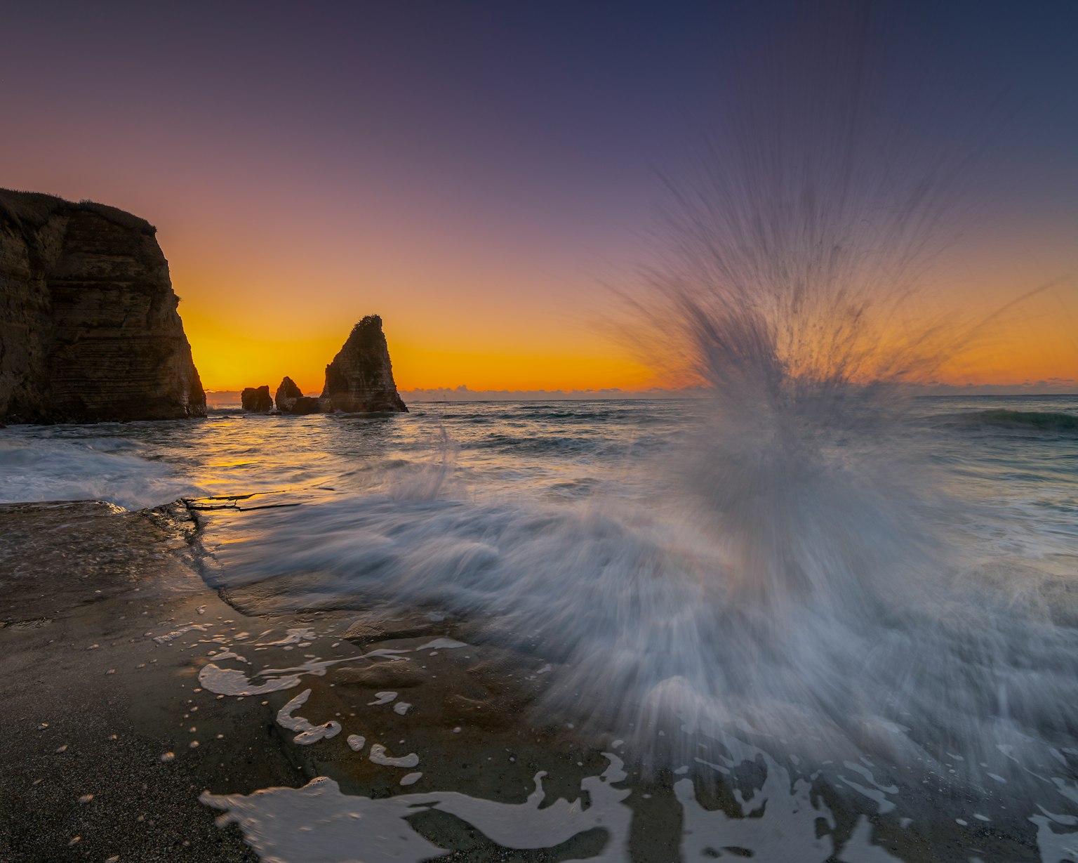Tramonto costiero con rocce e onde che schizzano