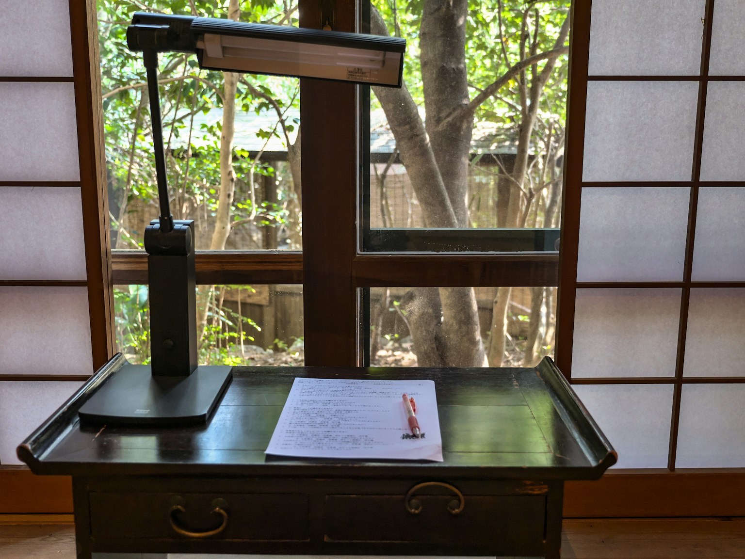 Un bureau en bois avec un document et une lampe Une vue de verdure à travers la fenêtre
