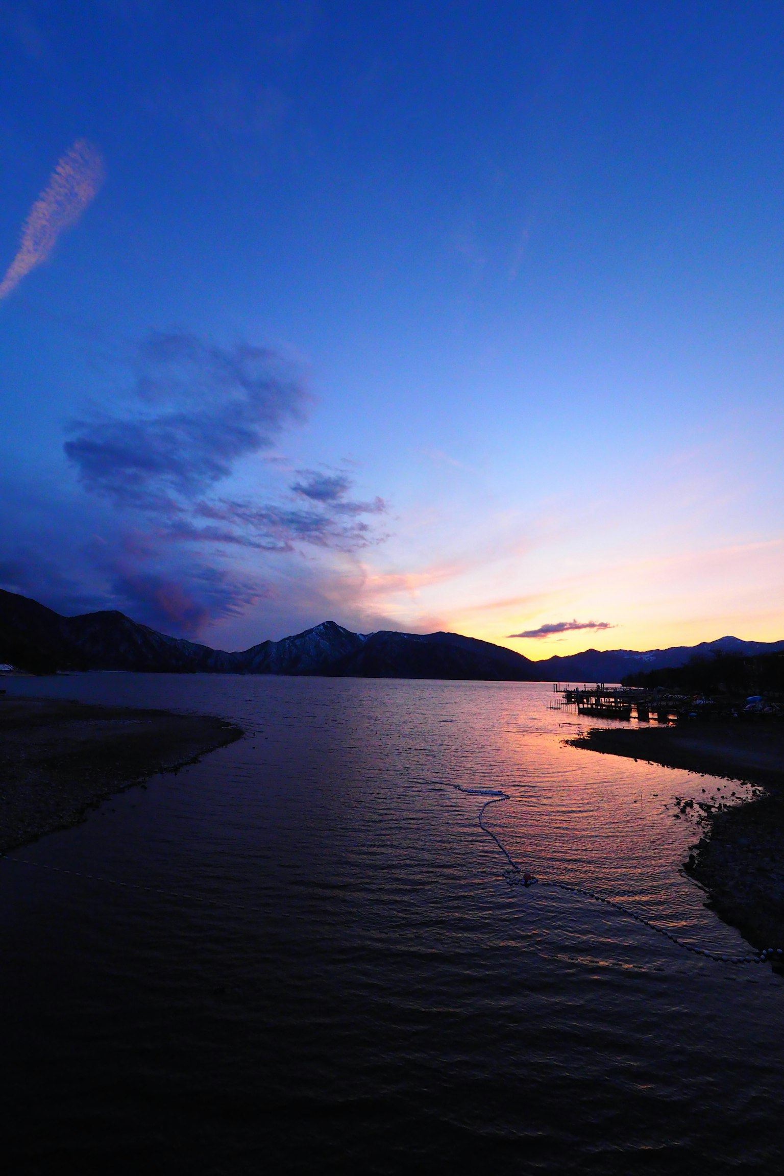 Pemandangan matahari terbenam yang indah di atas danau dengan refleksi gunung dan langit berwarna