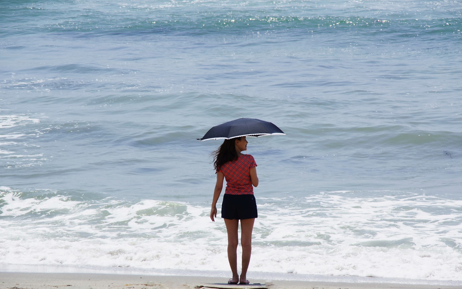 Une femme se tenant au bord de la mer avec un parapluie regardant les vagues