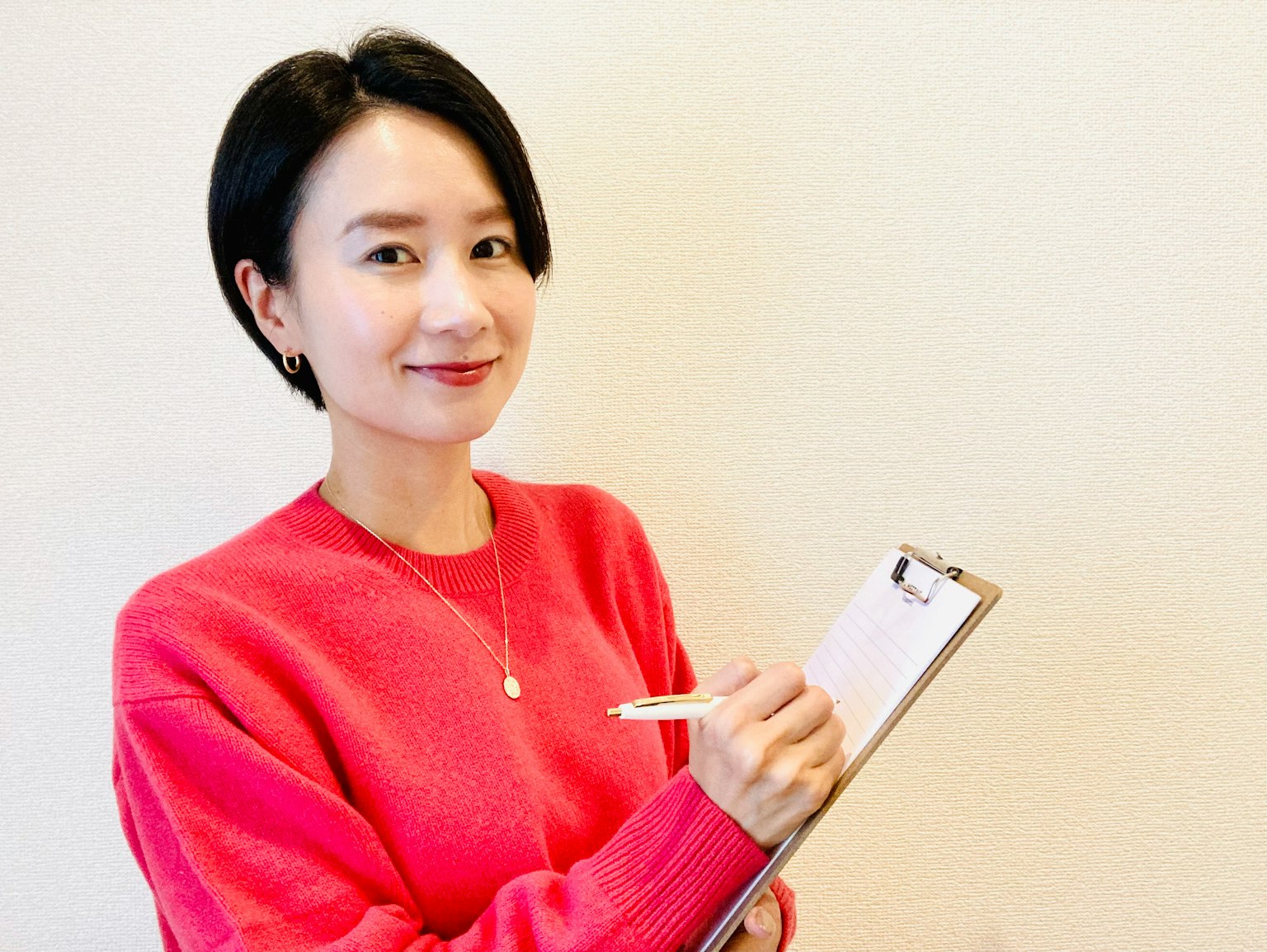Una donna in maglione rosa che tiene un clipboard e una penna sorridendo