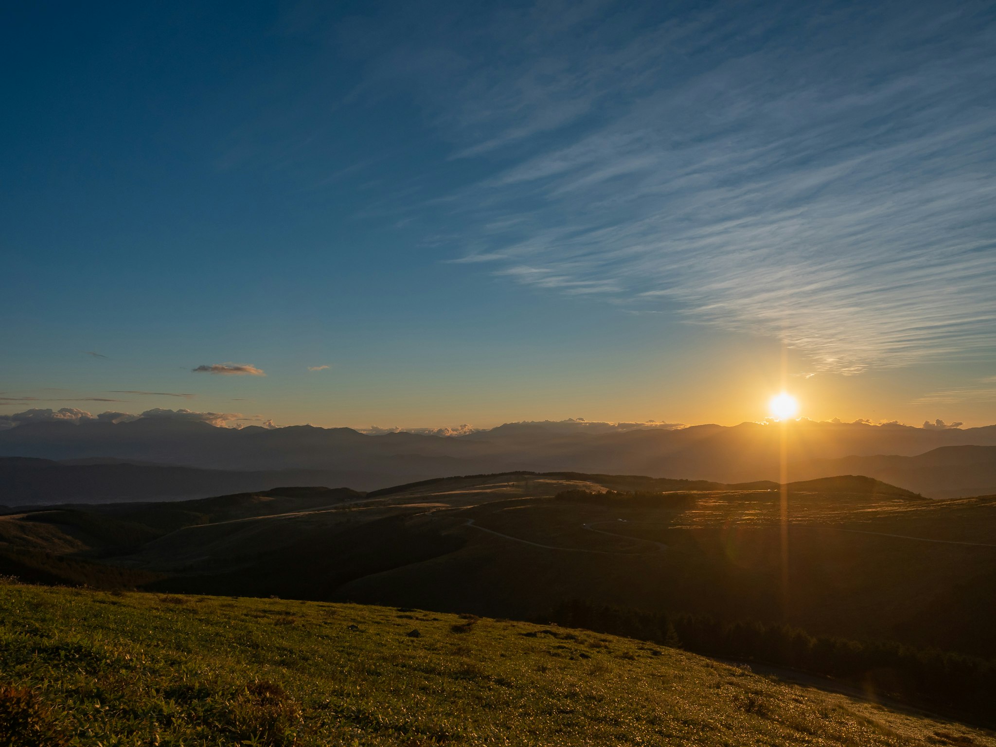夕日に照らされる丘陵の草原と山並み