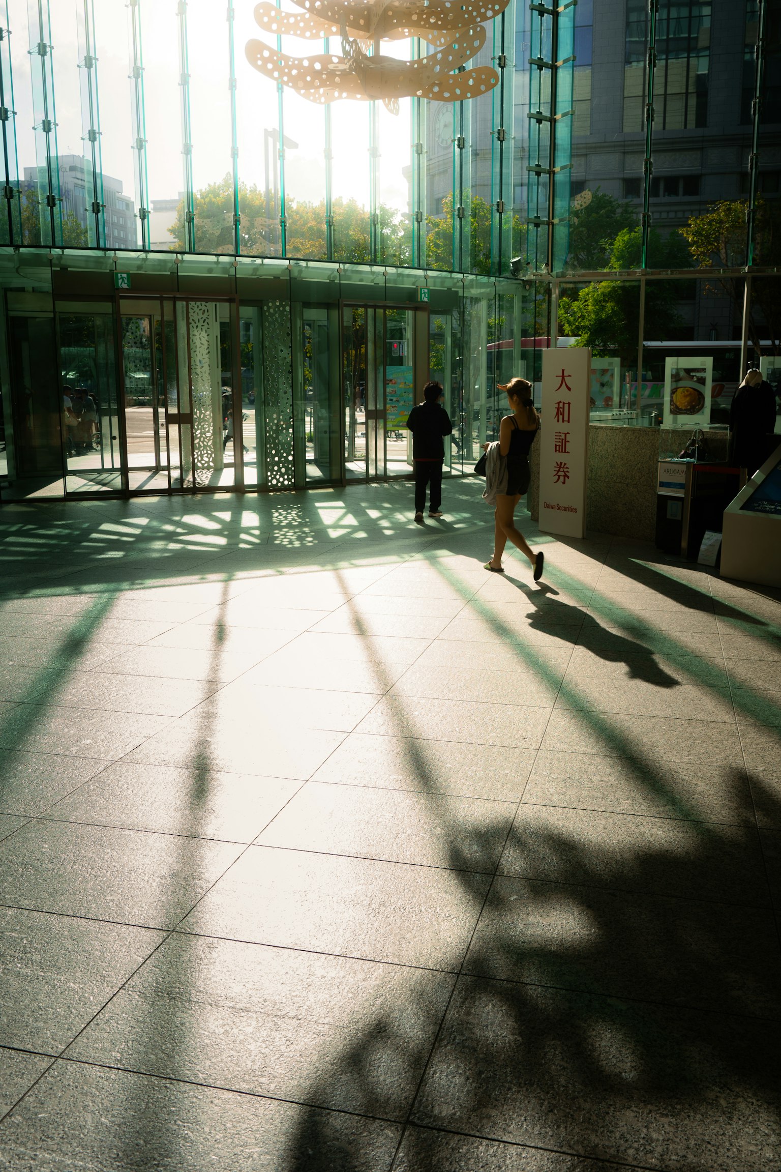 A woman walking in a brightly lit entrance with shadows on the floor