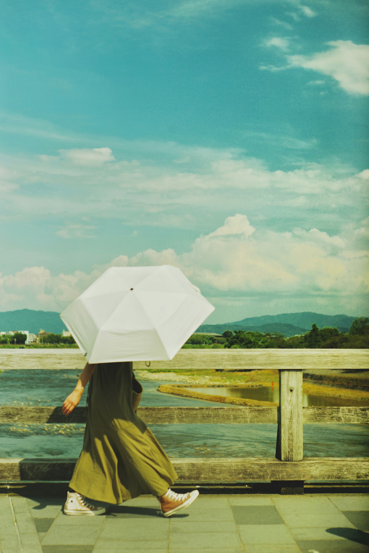 一位女性在藍天下走著,手持白色雨傘