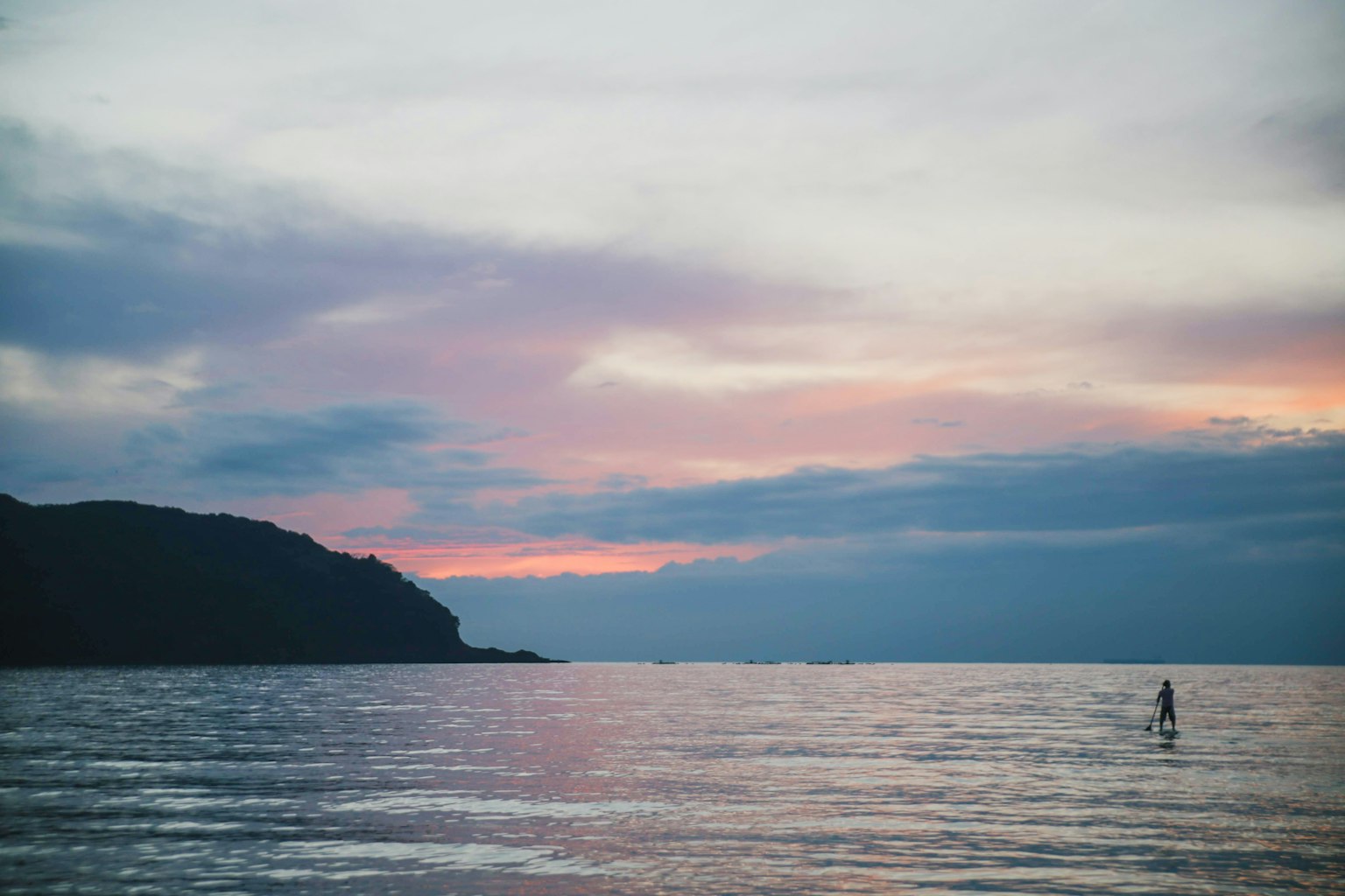 Persona che fa surf al tramonto su un mare calmo