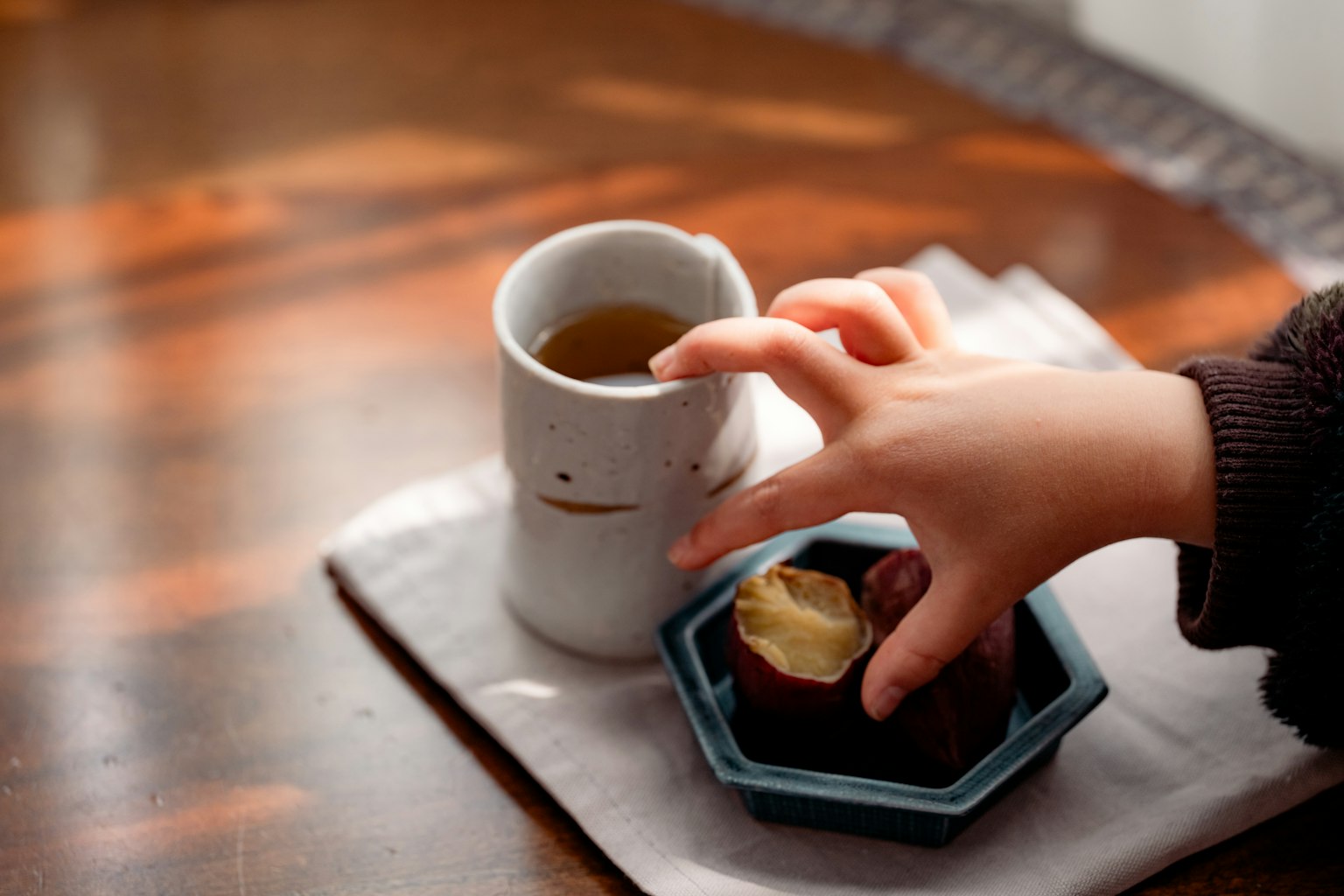 A hand reaching for sweets beside a cup of tea