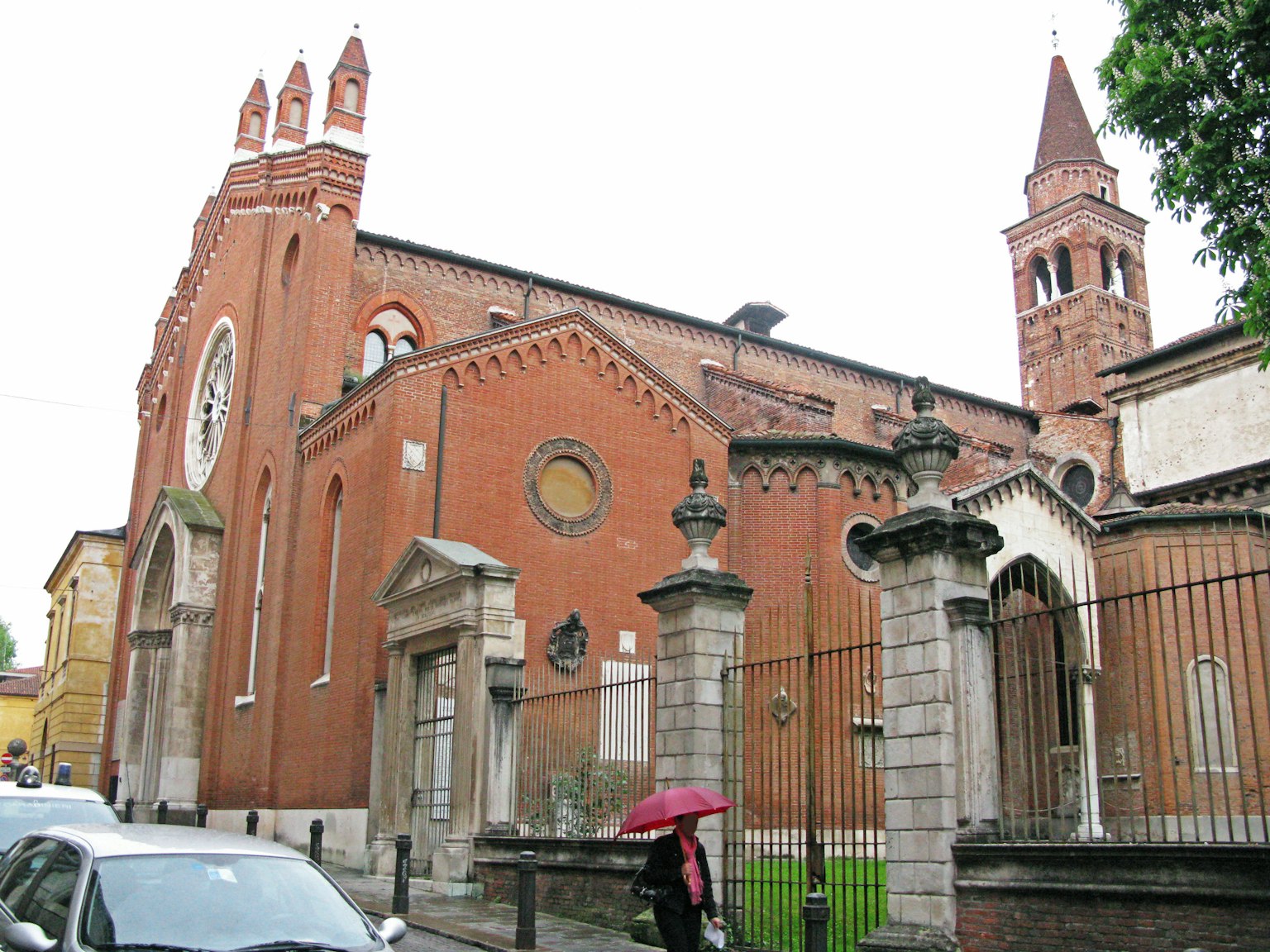 Église en briques rouges avec des bâtiments environnants par un jour de pluie avec une personne tenant un parapluie