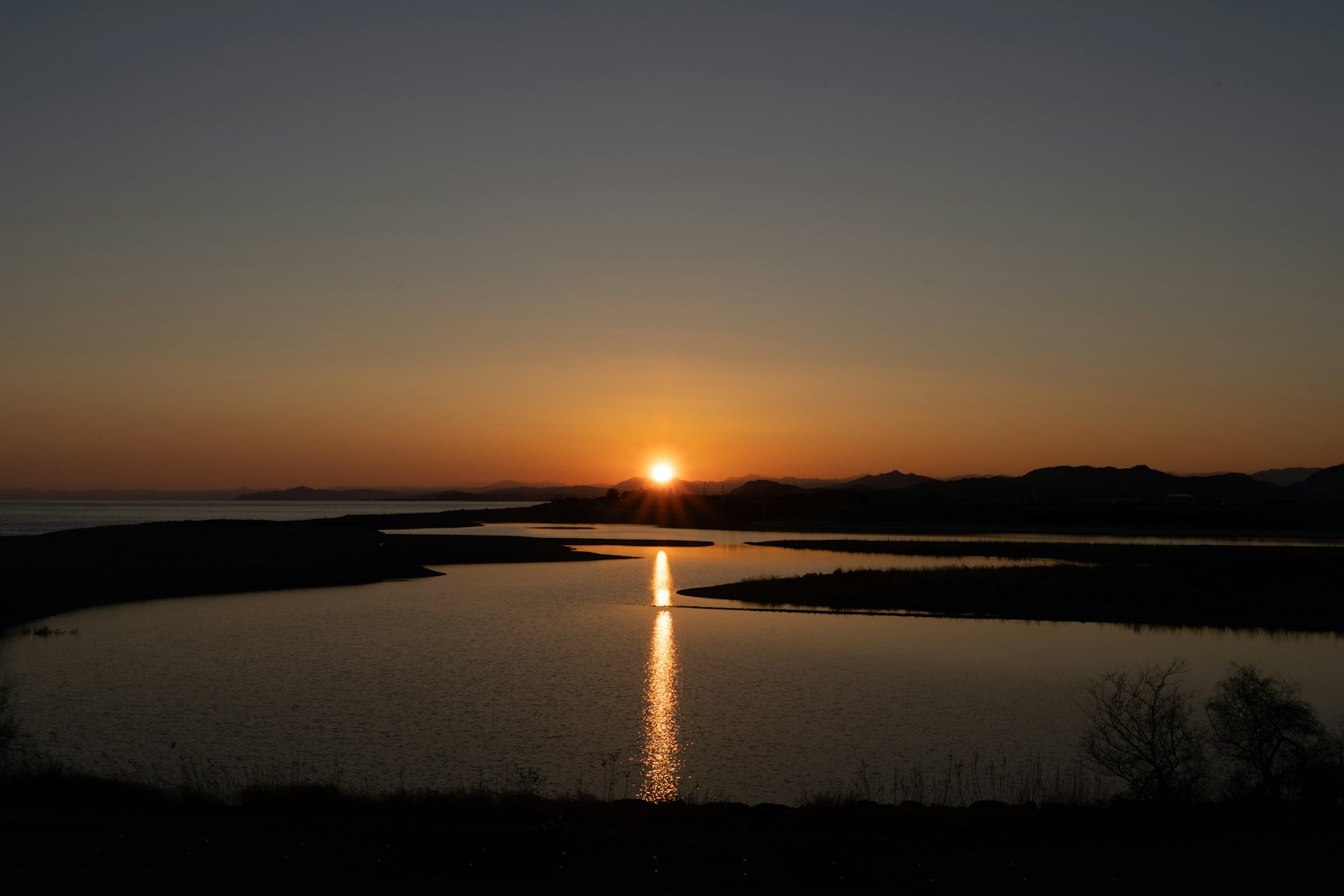 Sonnenuntergang über einem ruhigen See mit der Sonne, die am Horizont sinkt