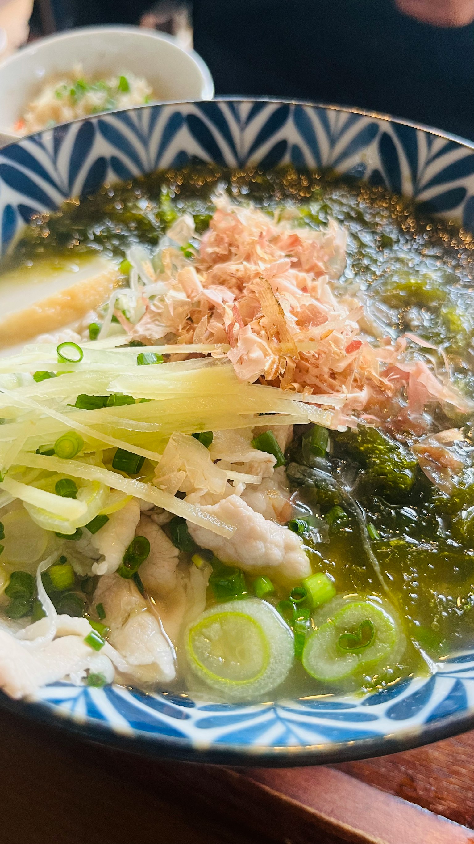 一碗绿色汤，上面撒有葱和 bonito 鱼片