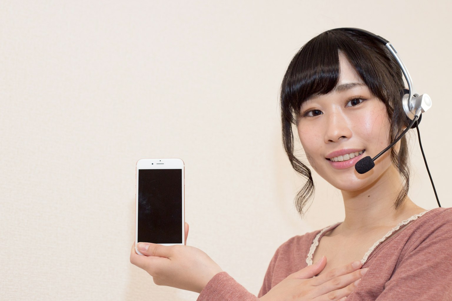 A woman wearing a headset holding a smartphone and smiling