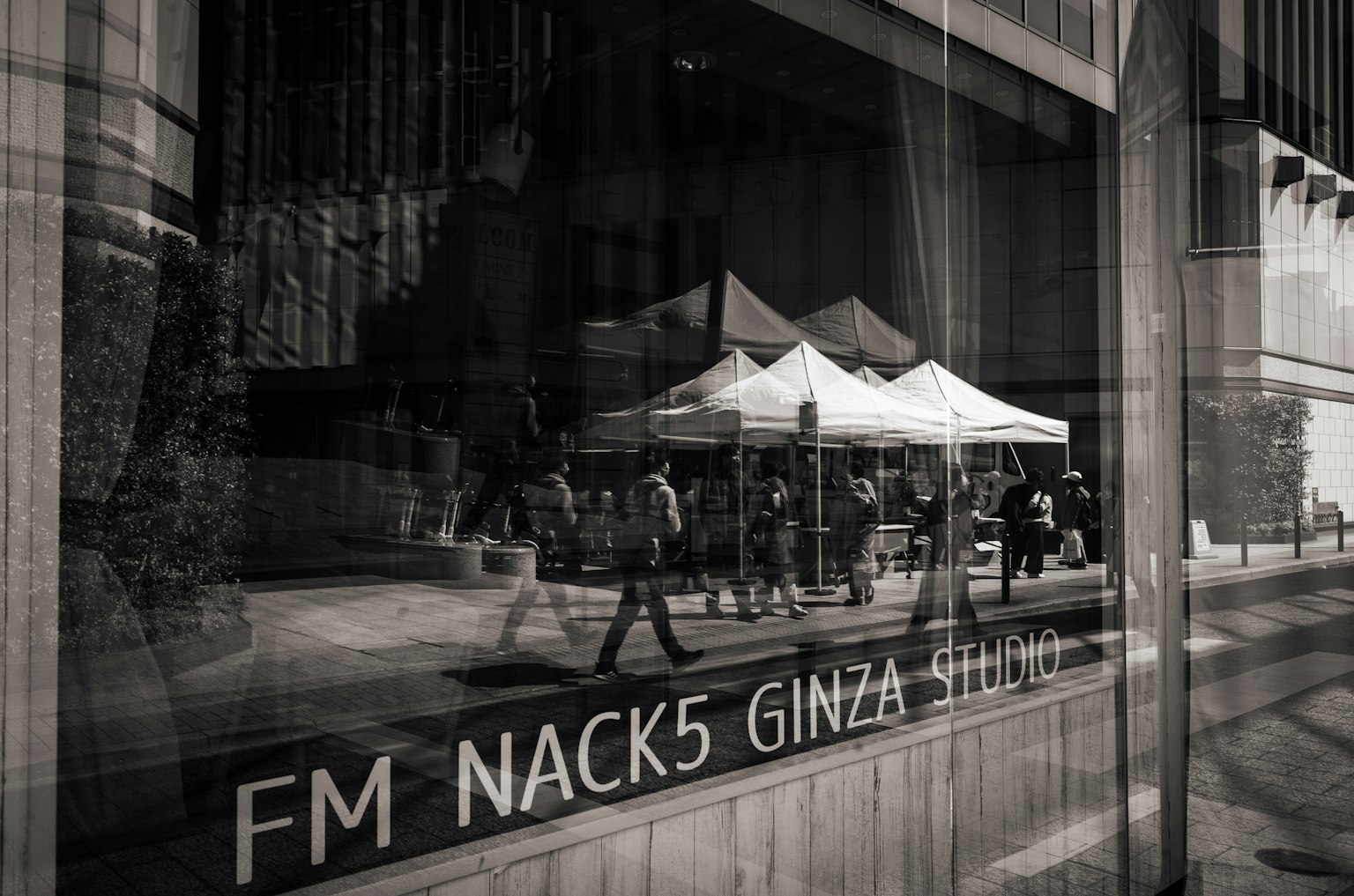 Ảnh đen trắng hiển thị biển hiệu FM NACK5 cùng mọi người bên ngoài