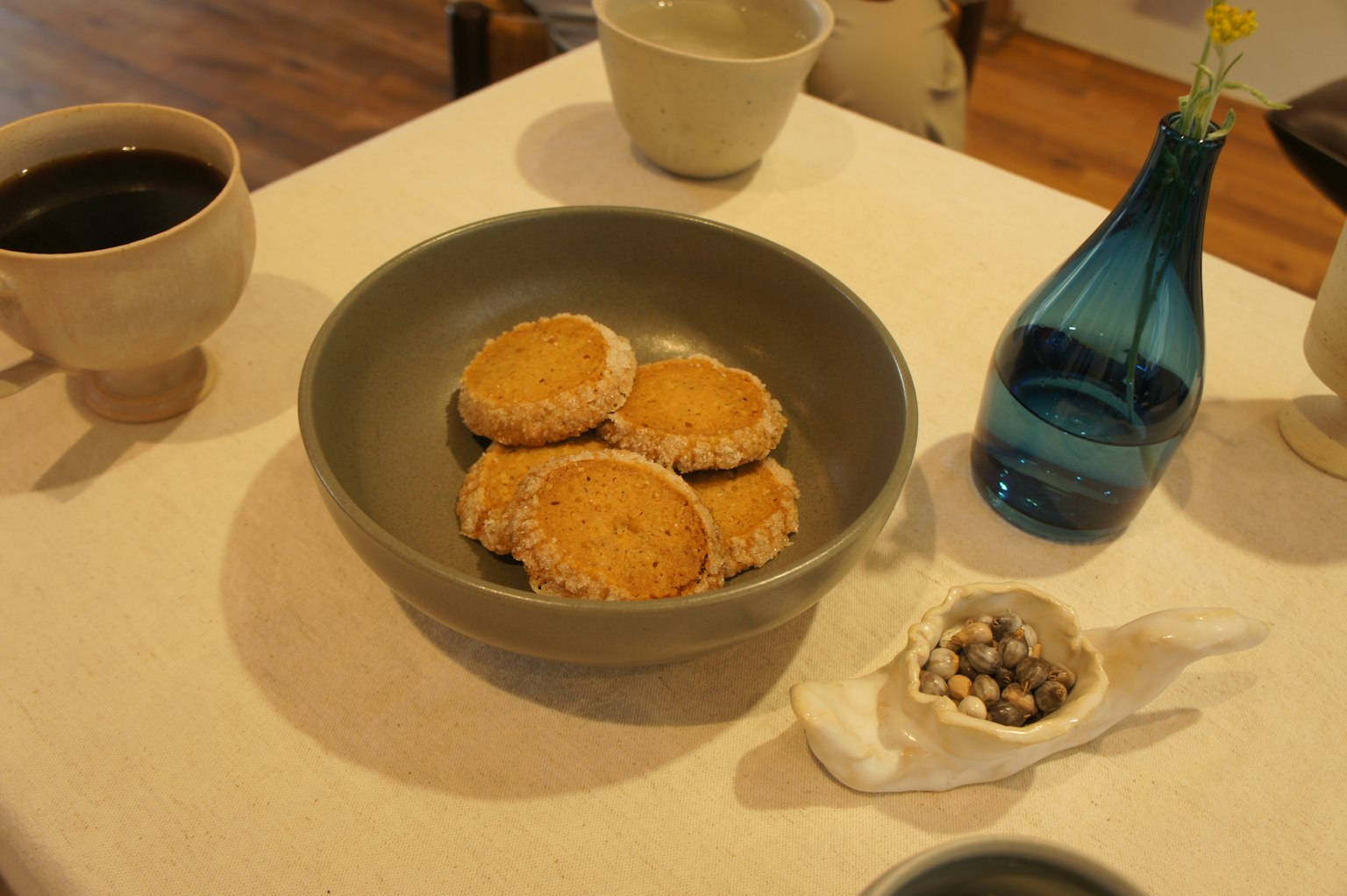 ชามสีเทาที่มีคุกกี้อยู่บนโต๊ะข้างแก้วกาแฟและแจกันสีน้ำเงิน