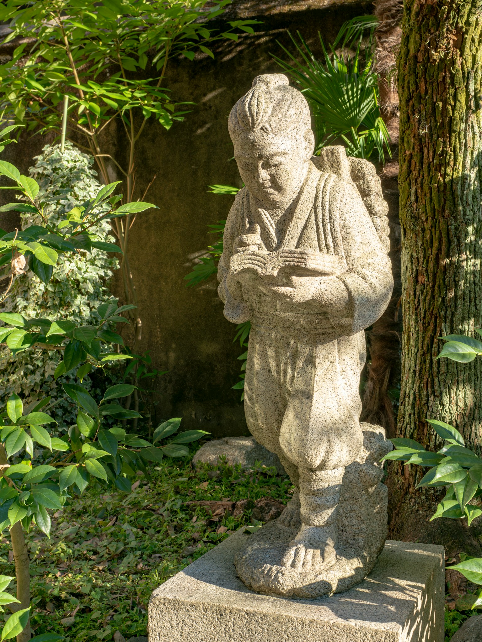 Stone statue of a child reading a book in a garden