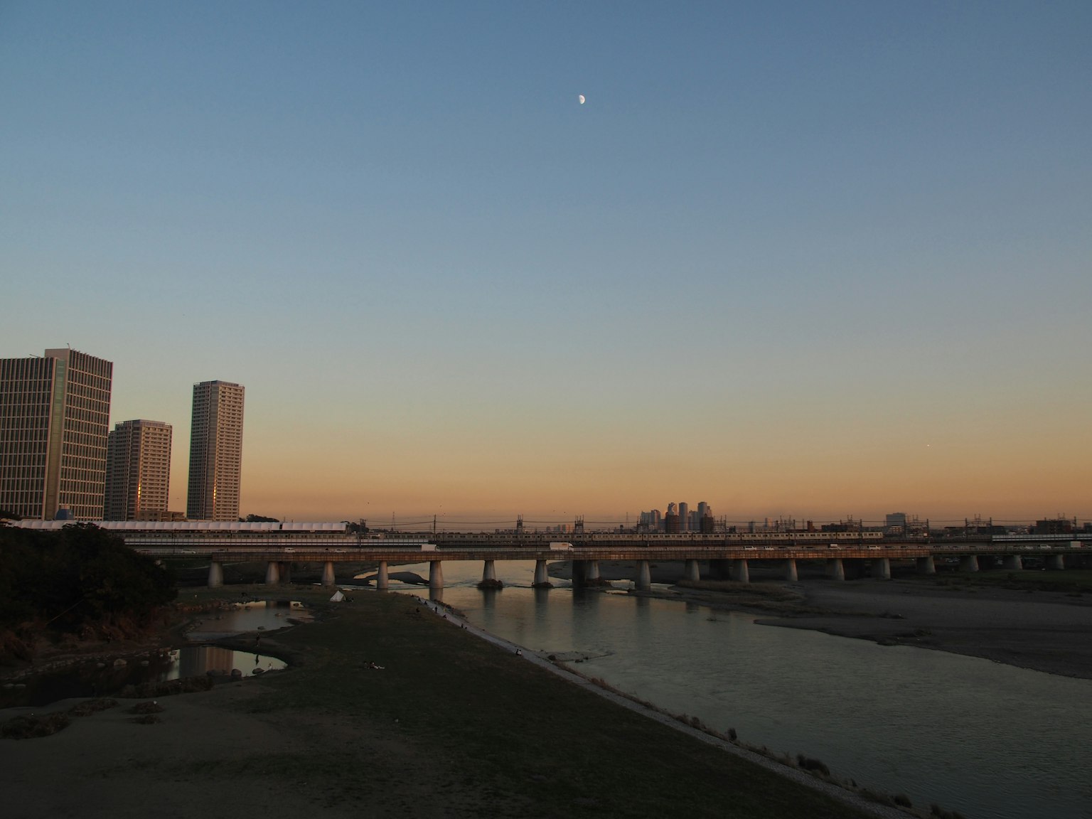 ทิวทัศน์เมืองในยามพลบค่ำพร้อมแม่น้ำและสะพานในพื้นหน้า